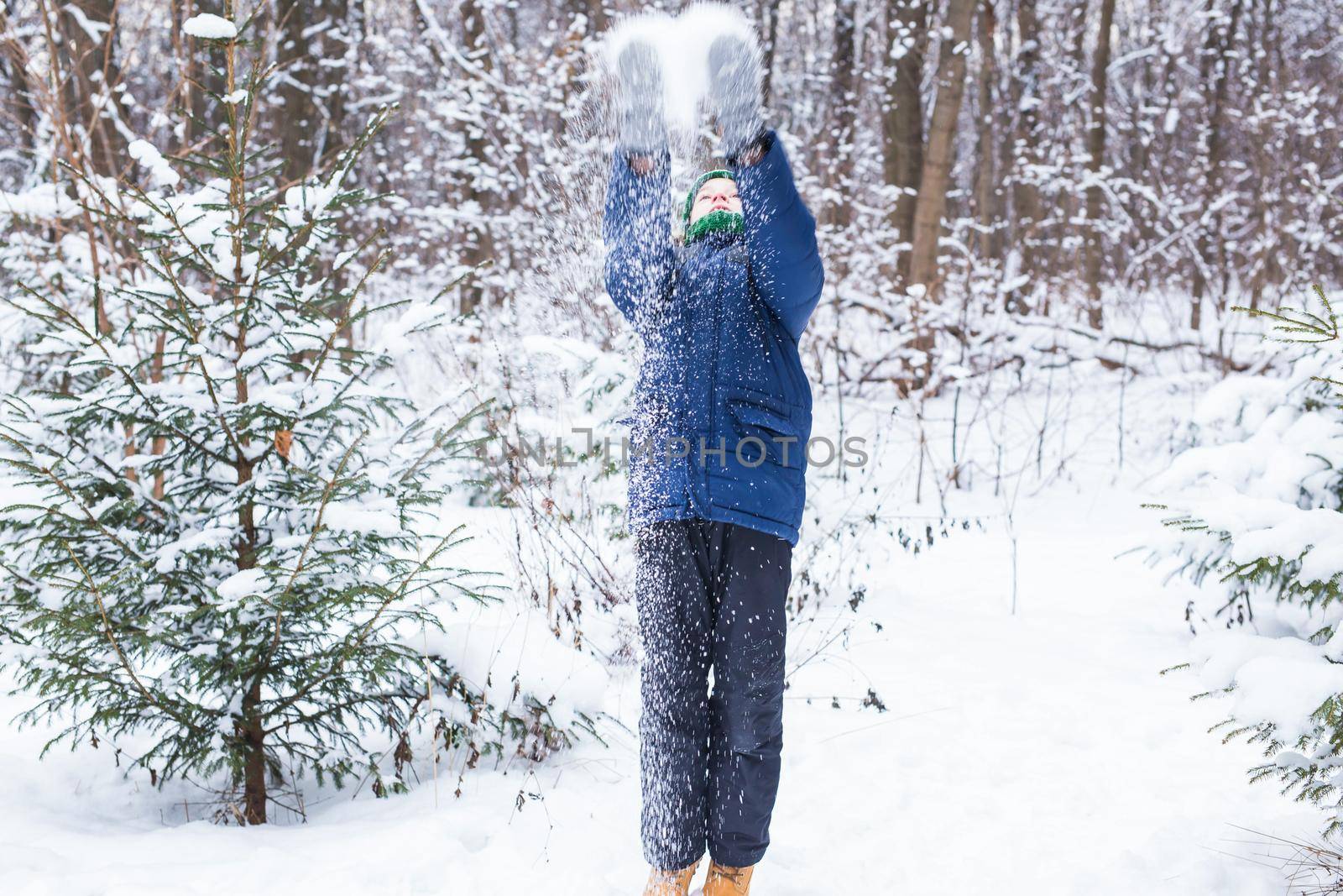 Young boy plays with snow, have fun, smiles. Teenager in winter park. Active lifestyle, winter activity, outdoor winter games, snowballs.