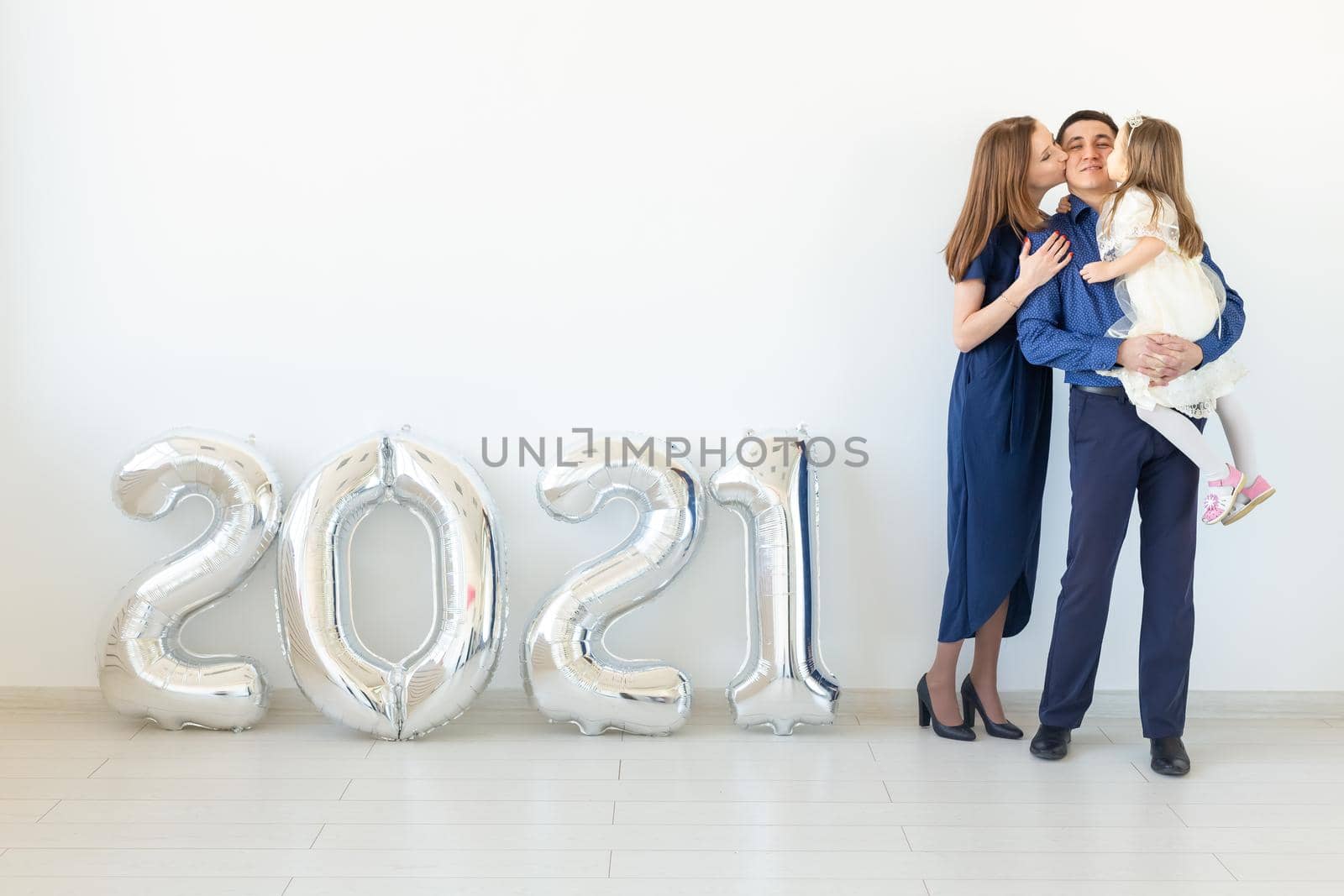 Young happy family mother and father and daughter standing near balloons shaped like numbers 2021 on white background. New year, Christmas, holiday by Satura86