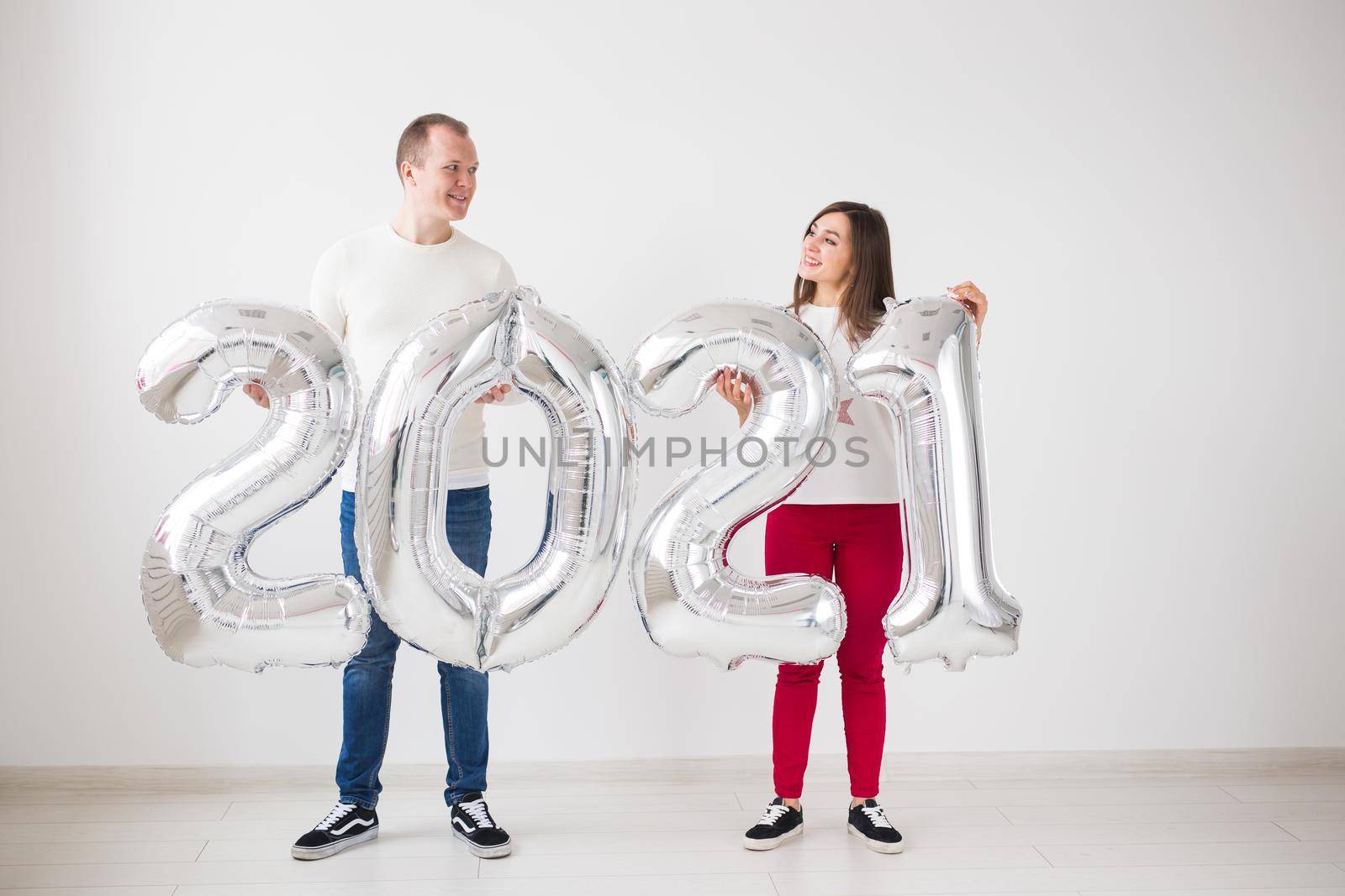 New 2021 Year is coming concept - Happy young man and woman are holding silver colored numbers indoors. by Satura86