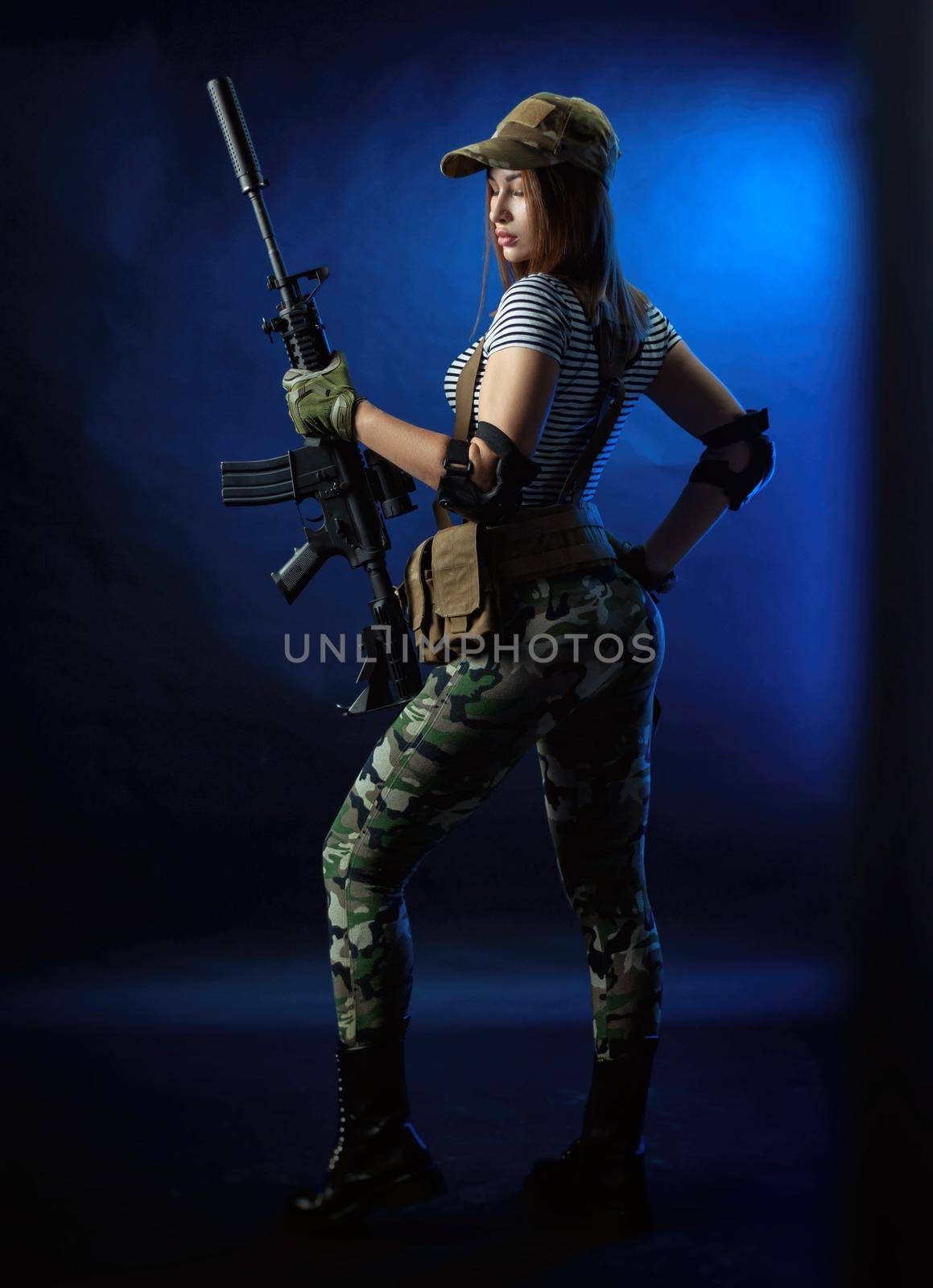 the woman in a military airsoft uniform in a vest with an American automatic rifle on a dark background