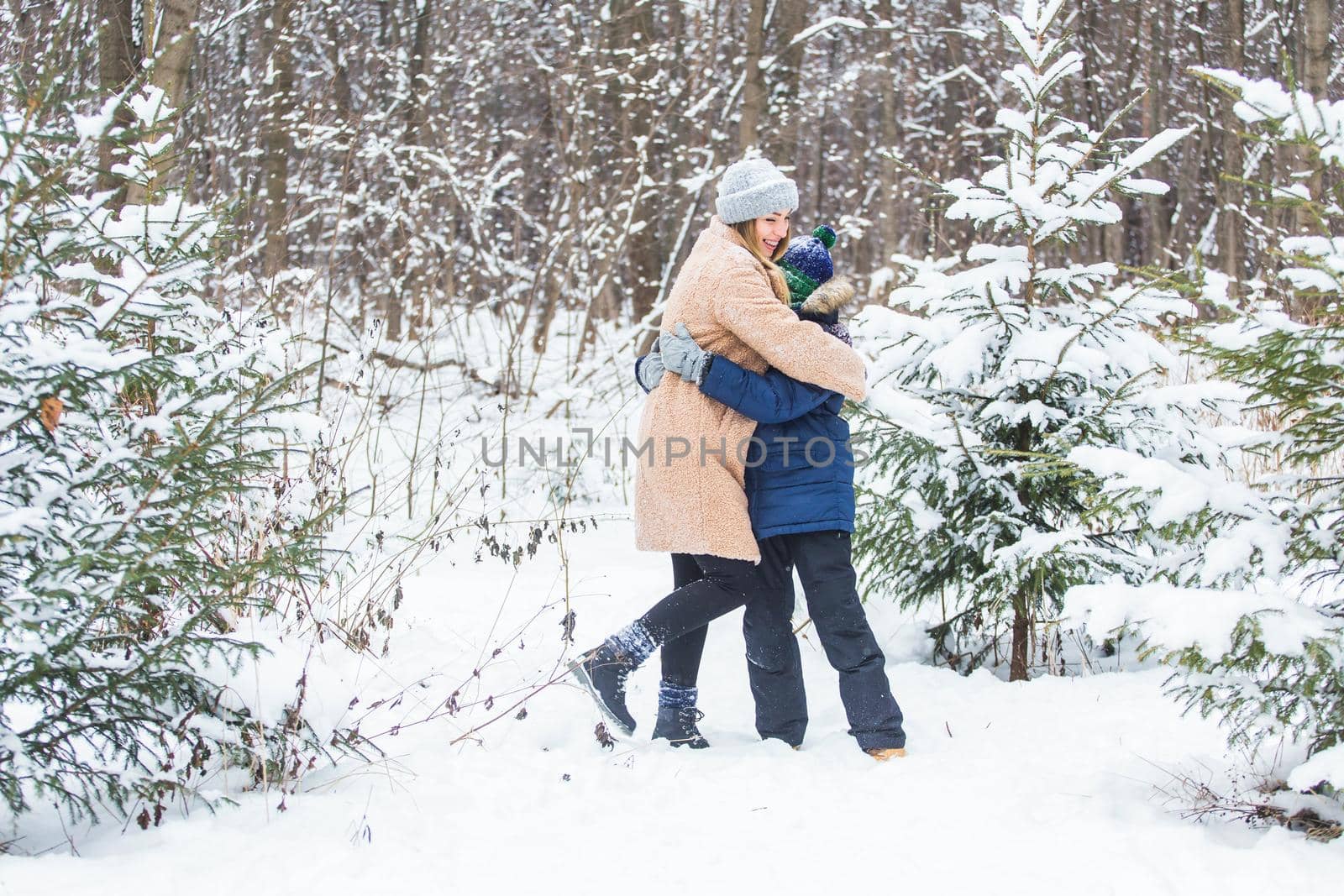 Parenting, fun and season concept - Happy mother and son having fun and playing with snow in winter forest.