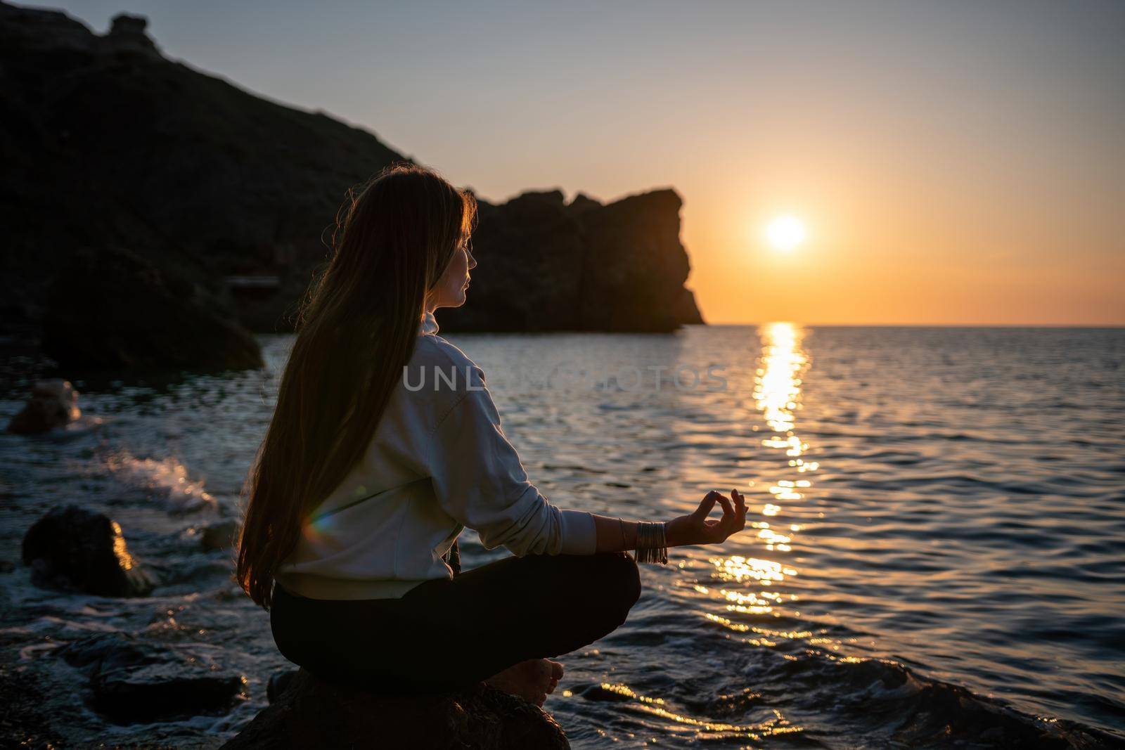 Young woman in swimsuit with long hair practicing stretching outdoors on yoga mat by the sea on a sunny day. Women's yoga fitness pilates routine. Healthy lifestyle, harmony and meditation concept.