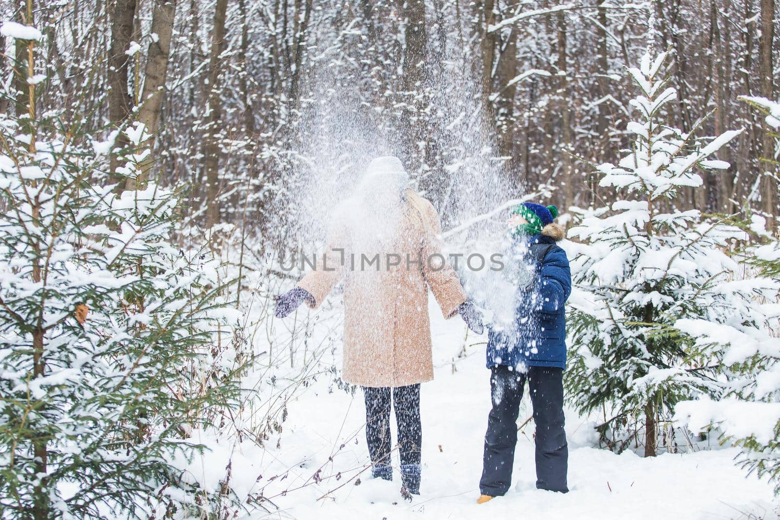 Parenting, fun and season concept - Happy mother and son having fun and playing with snow in winter forest.