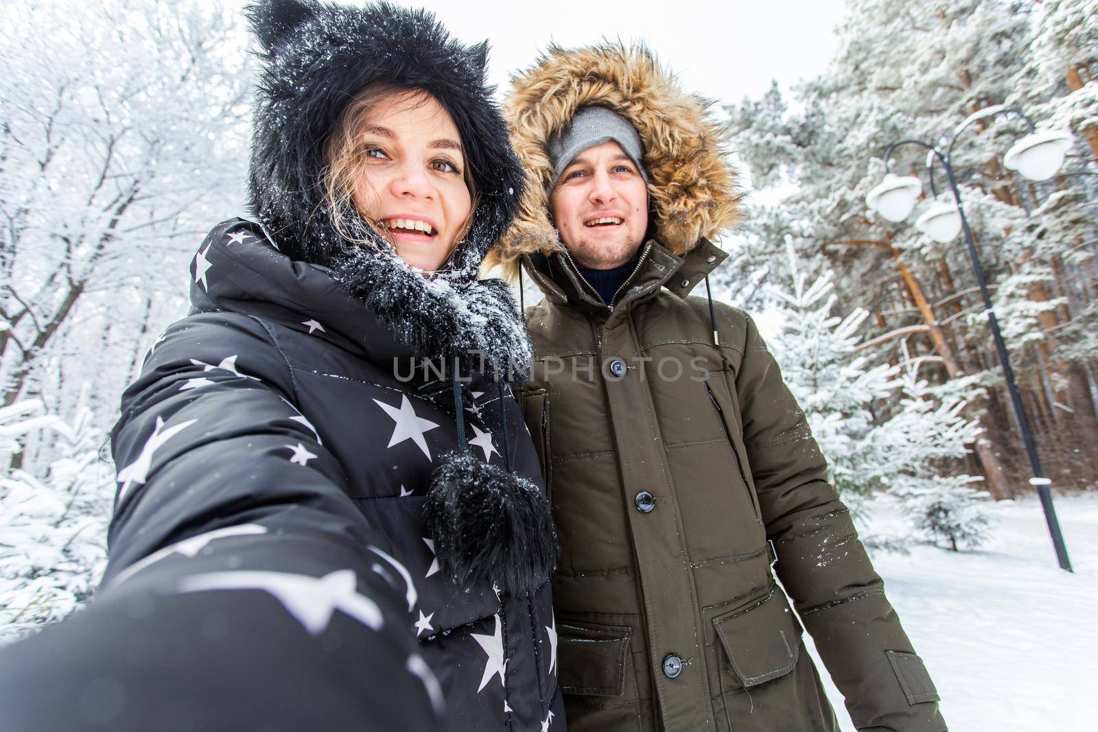 Technologies and relationship concept - Happy smiling couple taking a selfie in a winter forest outside.