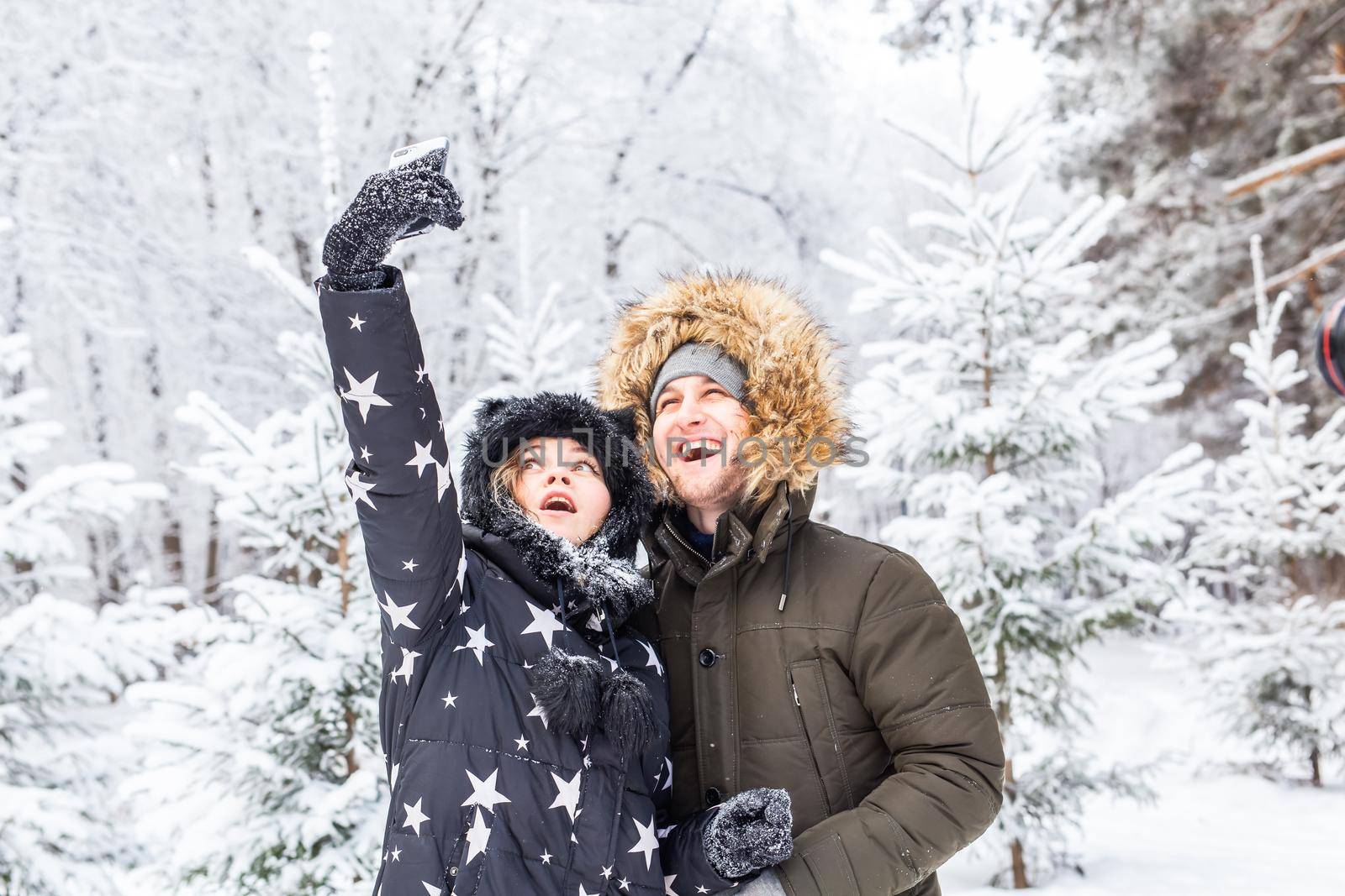 Technologies and relationship concept - Happy smiling couple taking a selfie in a winter forest outside.