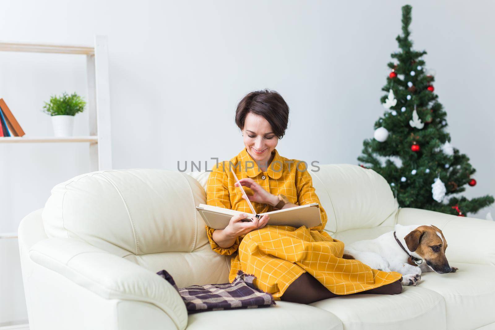 Woman reads book in front of Christmas tree with dog jack russell terrier. Christmas, holidays and pet. by Satura86