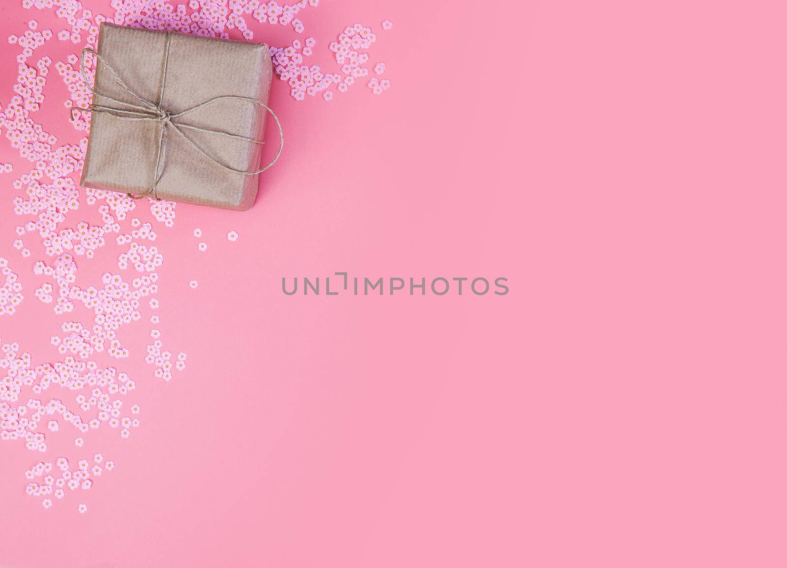 Gift box with brown Kraft paper surrounded with pink daisies and flatlay pink background, spring, Happy Mothers Day, Valentines Day and other Holliday concept top view, Modern design copy space