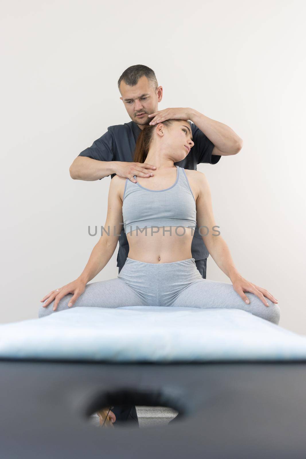 Chiropractic treatment - young woman sitting on the couch - the doctor turning her head to the side. Mid shot