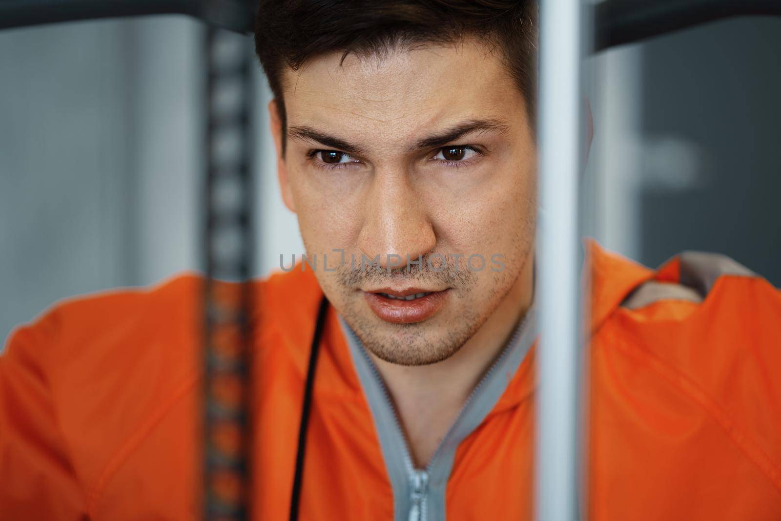 Young man in orange windbreaker working out training back muscles in the gym