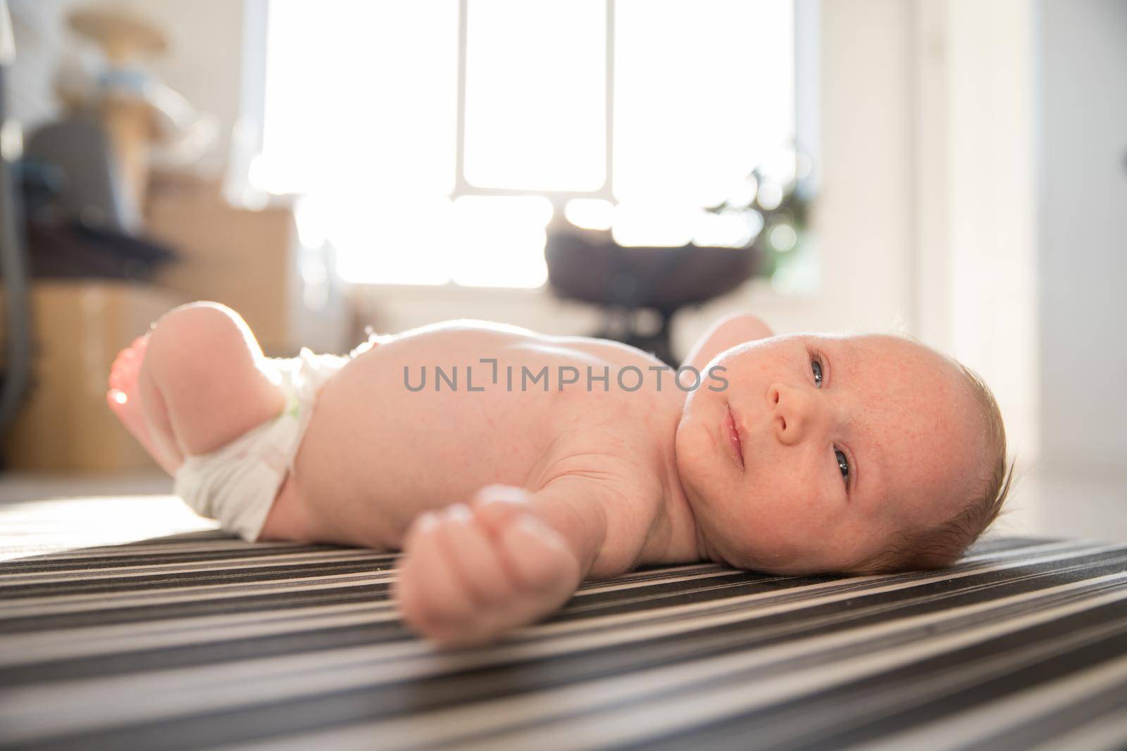 A little baby in a diaper restlessly lying on his back on striped sheets in day light. Mid shot
