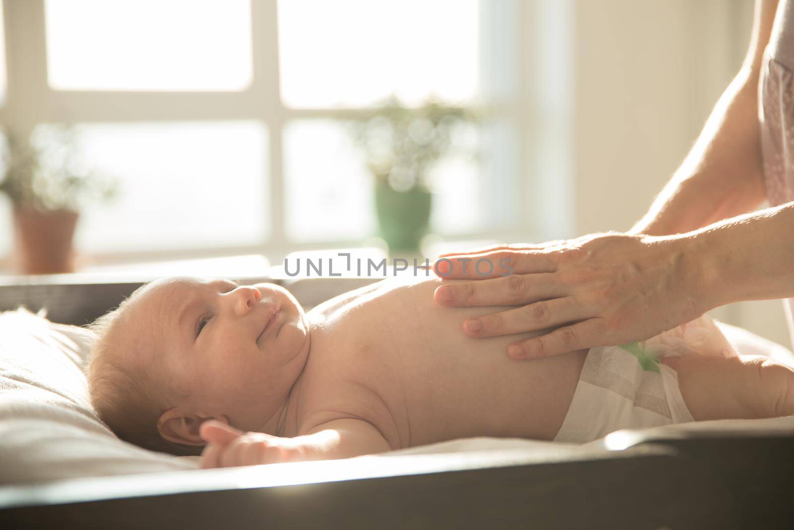 Mother with her hands on her smiling baby lying on a bed. Mid shot