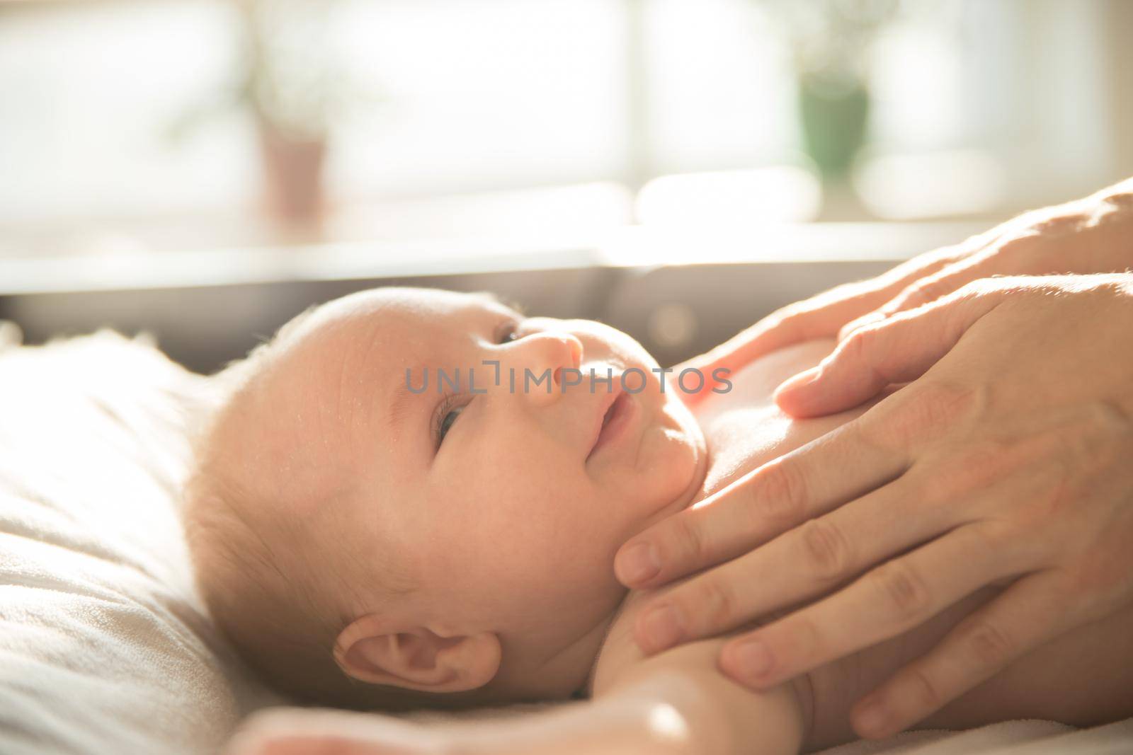 Mothers hands on her smiling baby lying on a bed. Mid shot