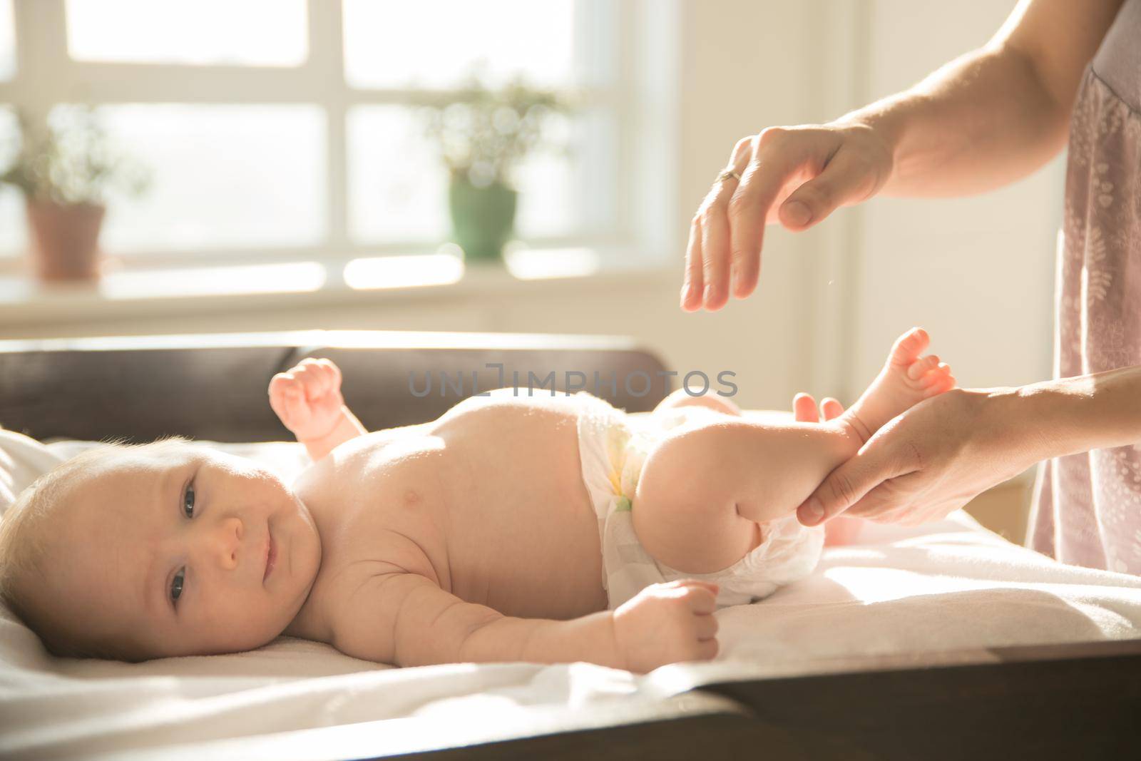 Mother massaging legs of her little baby lying on a bed. Mid shot