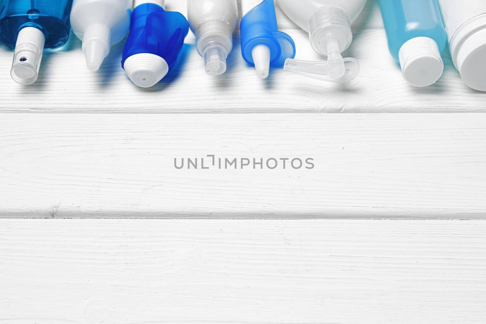 Row of bottles with hand sanitizers, liquid soap and medical preparations on white wooden background