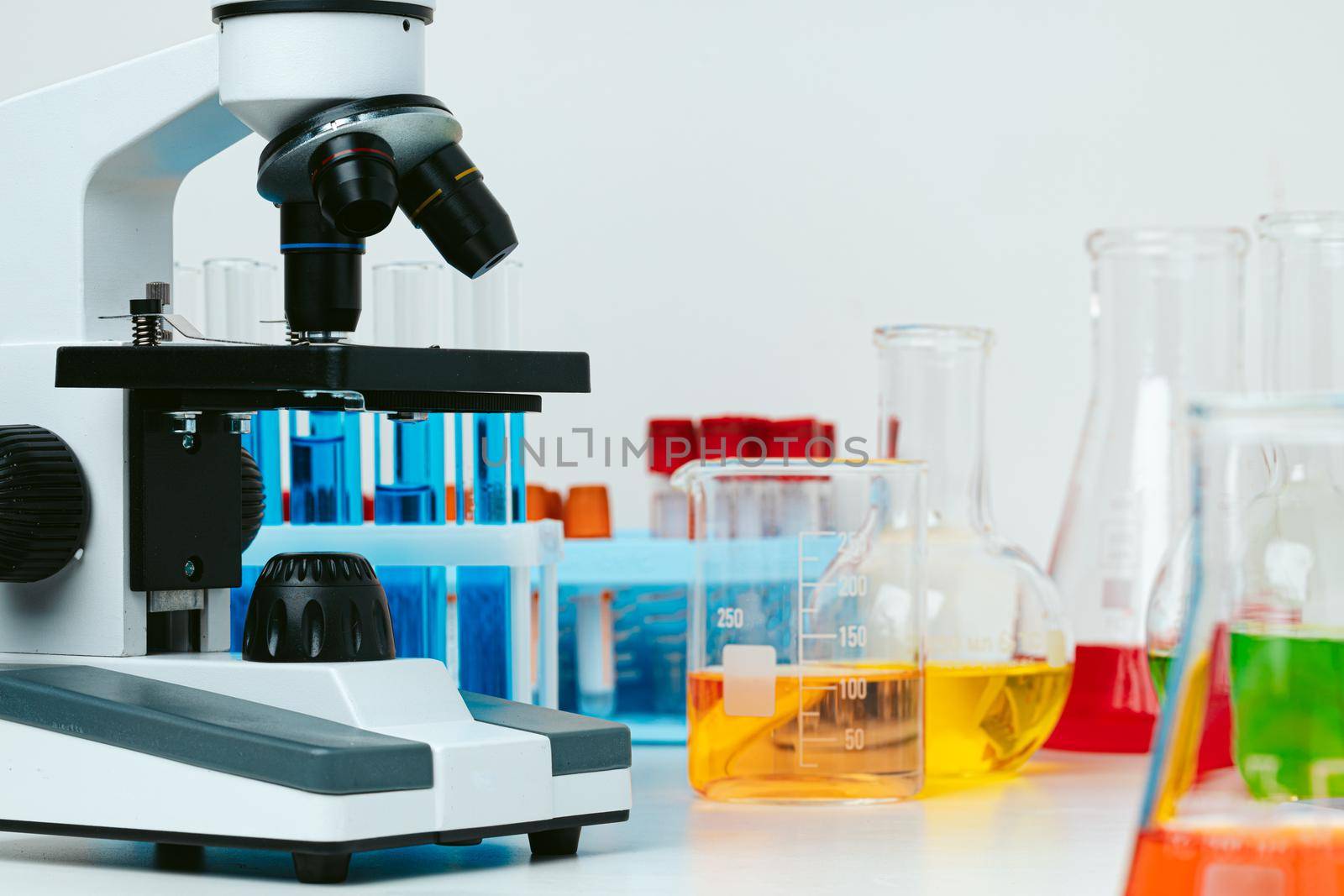 Microscope and colored test tubes on table in laboratory, close up
