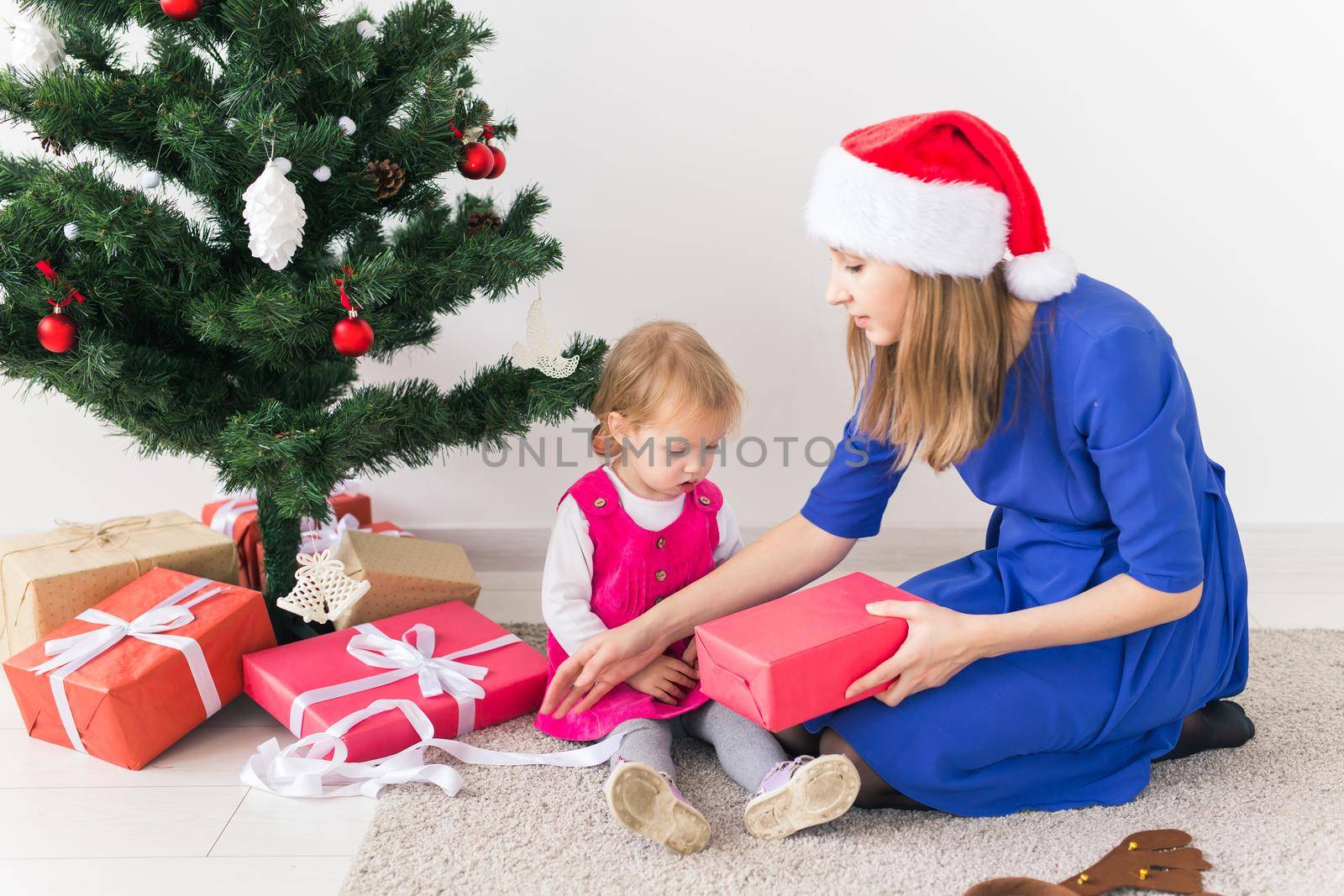 Smiling mother open Christmas presents with baby daughter in room at background. Winter season. Motherhood. Merry Christmas. New Year. by Satura86
