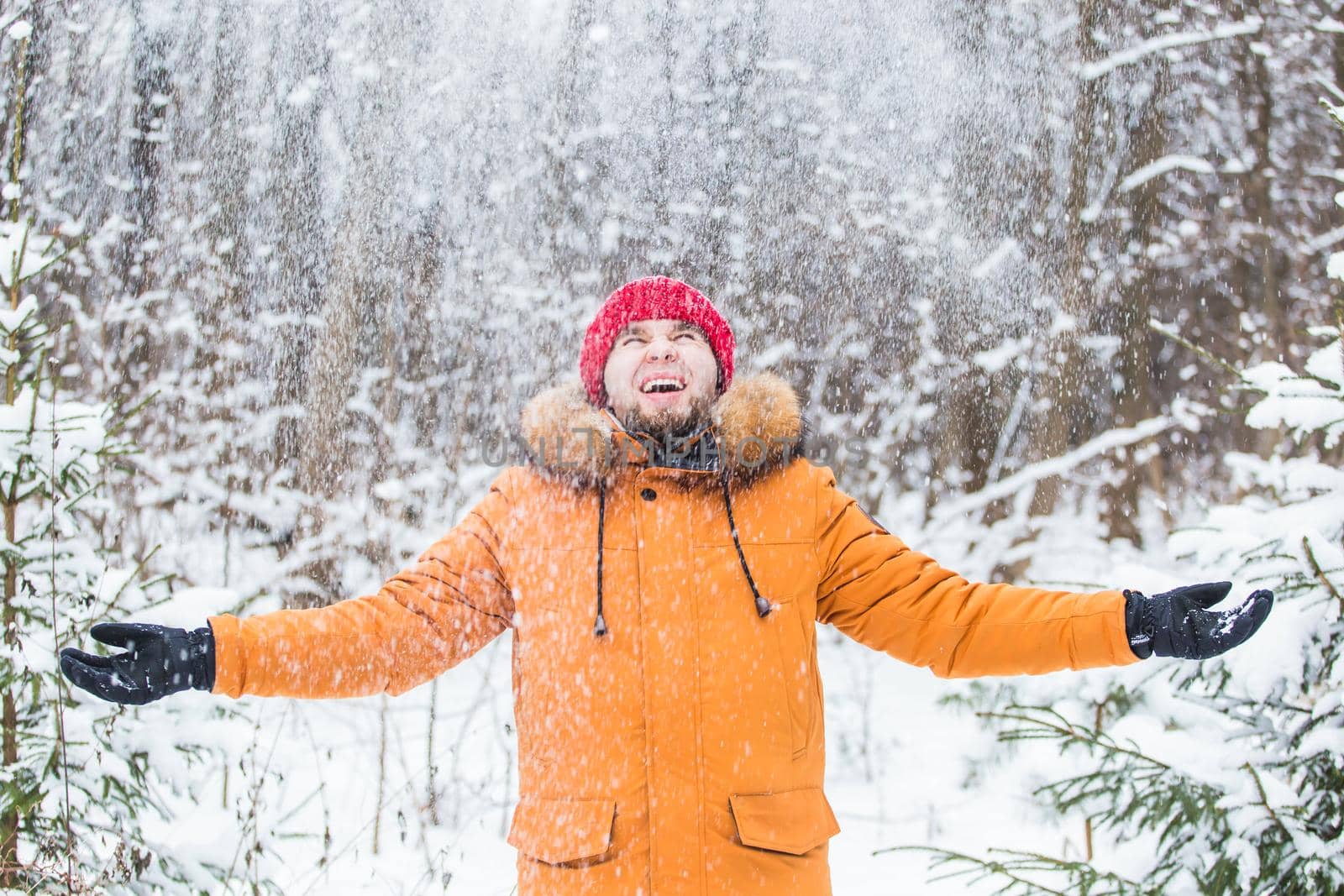 Young man throwing snow in winter forest. Guy having fun outdoors. Winter activities