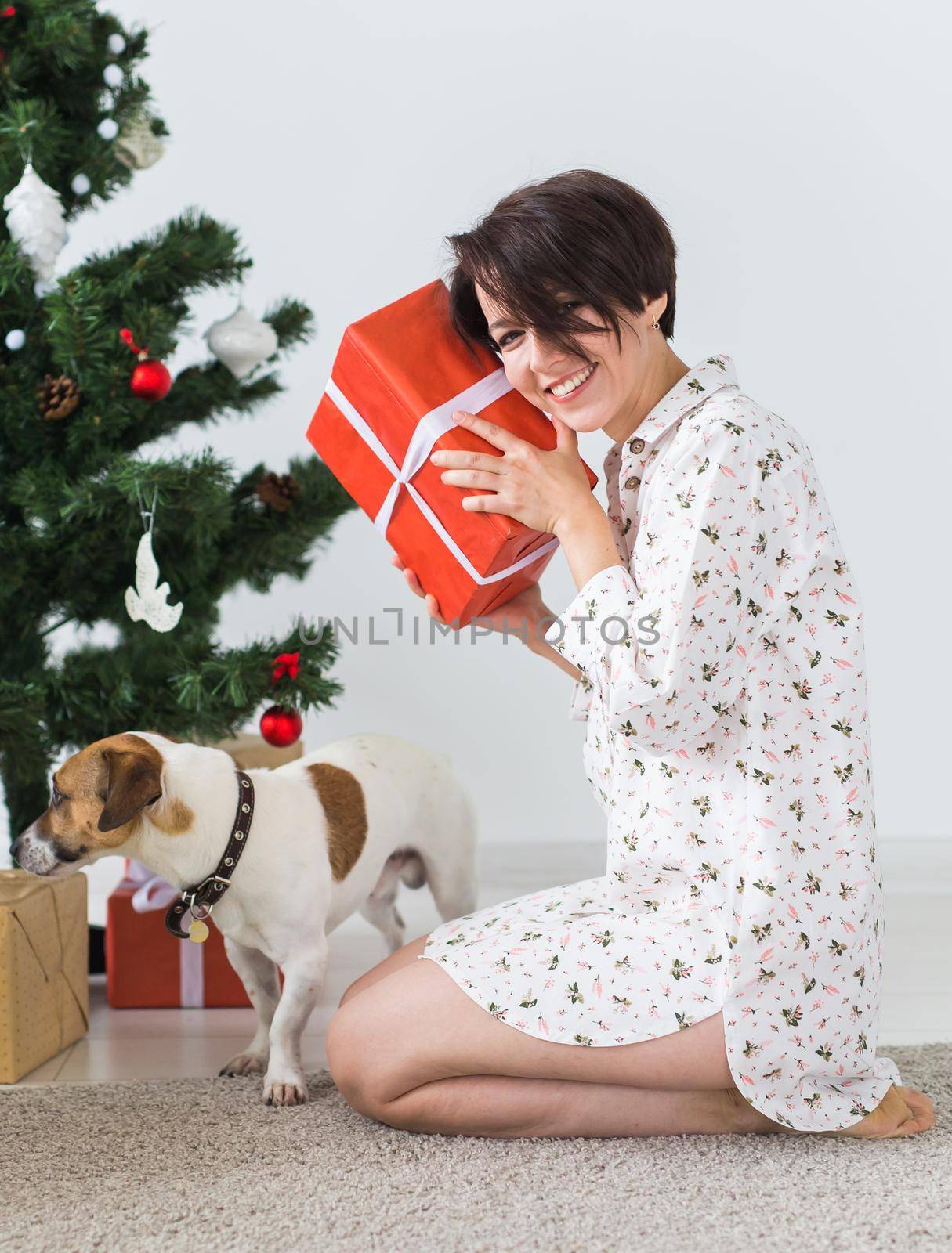 Happy young woman with lovely dog opening present box under christmas tree.