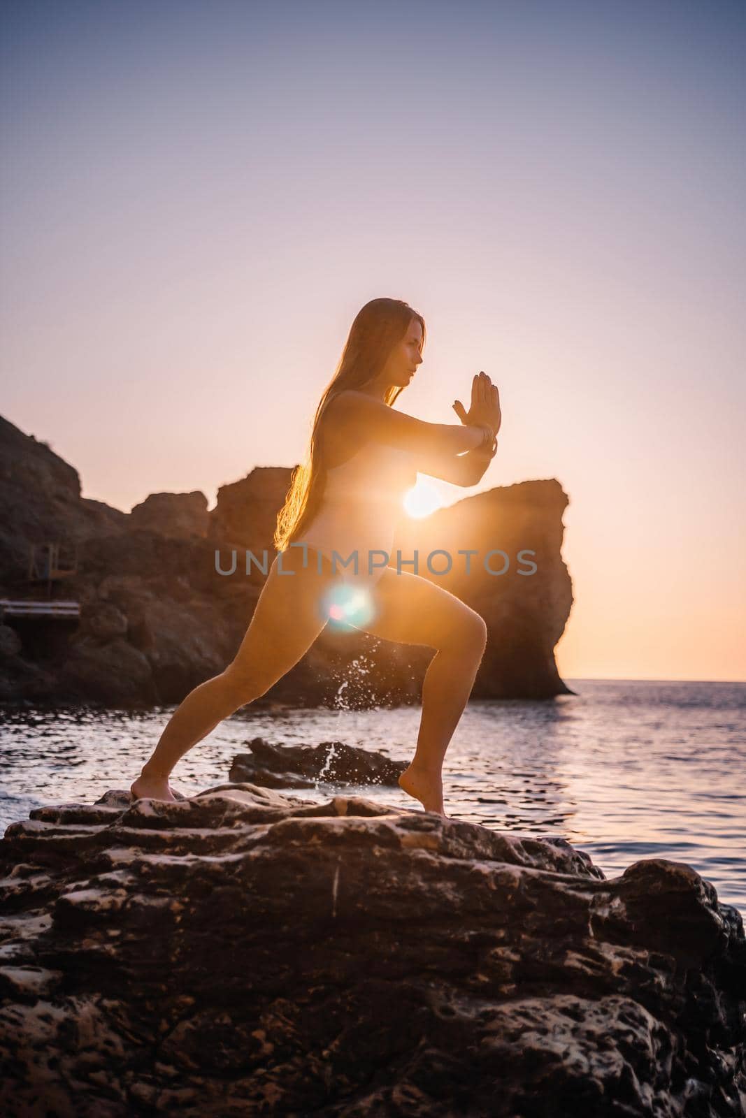 Young woman in swimsuit with long hair practicing stretching outdoors on yoga mat by the sea on a sunny day. Women's yoga fitness pilates routine. Healthy lifestyle, harmony and meditation concept.