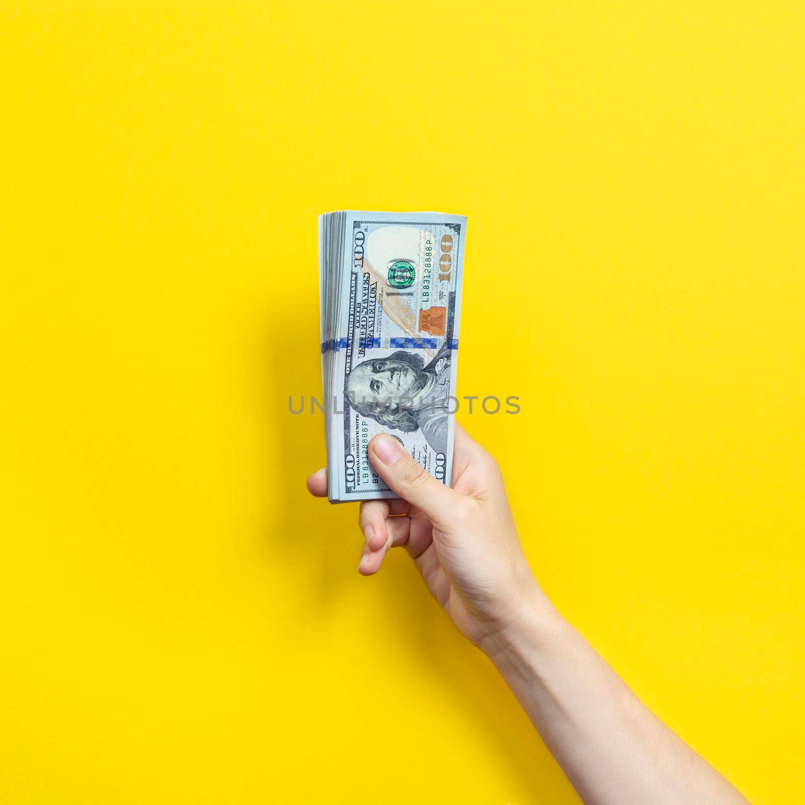 Hand holding a big stack of banknotes isolated on yellow background. Wealth or loan concept