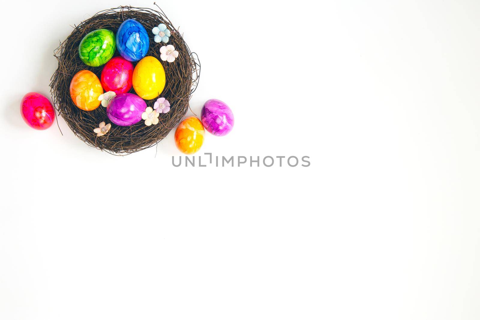 Colorful painted handmade Easter eggs in brown nest isolated on white background top view, Happy Easter holiday concept, with beautiful spring flowers copy space