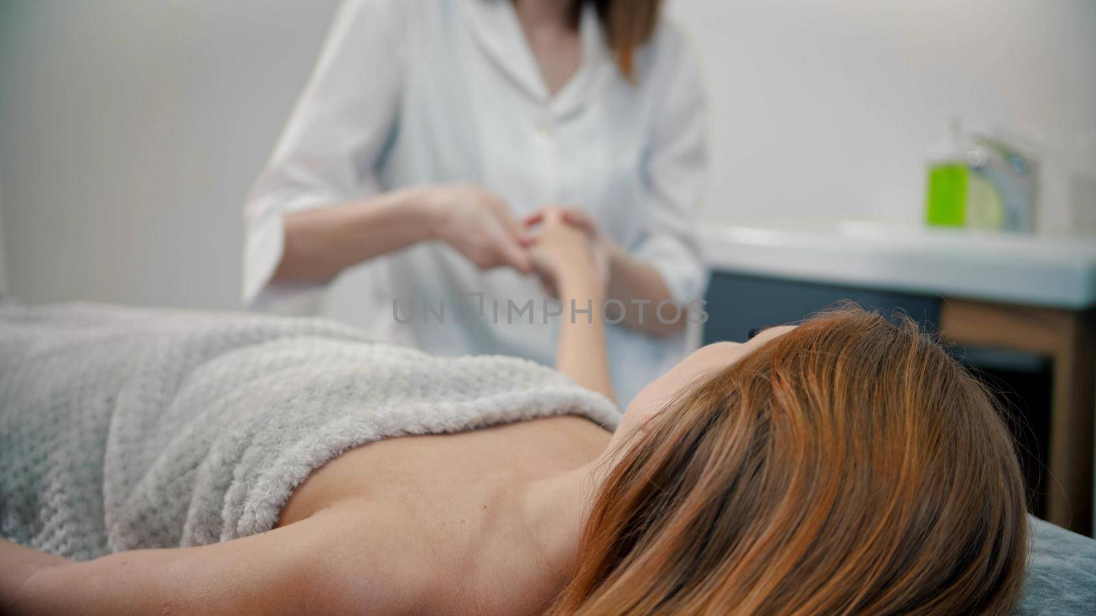 Female young massage therapist massaging hands of woman client - indoor