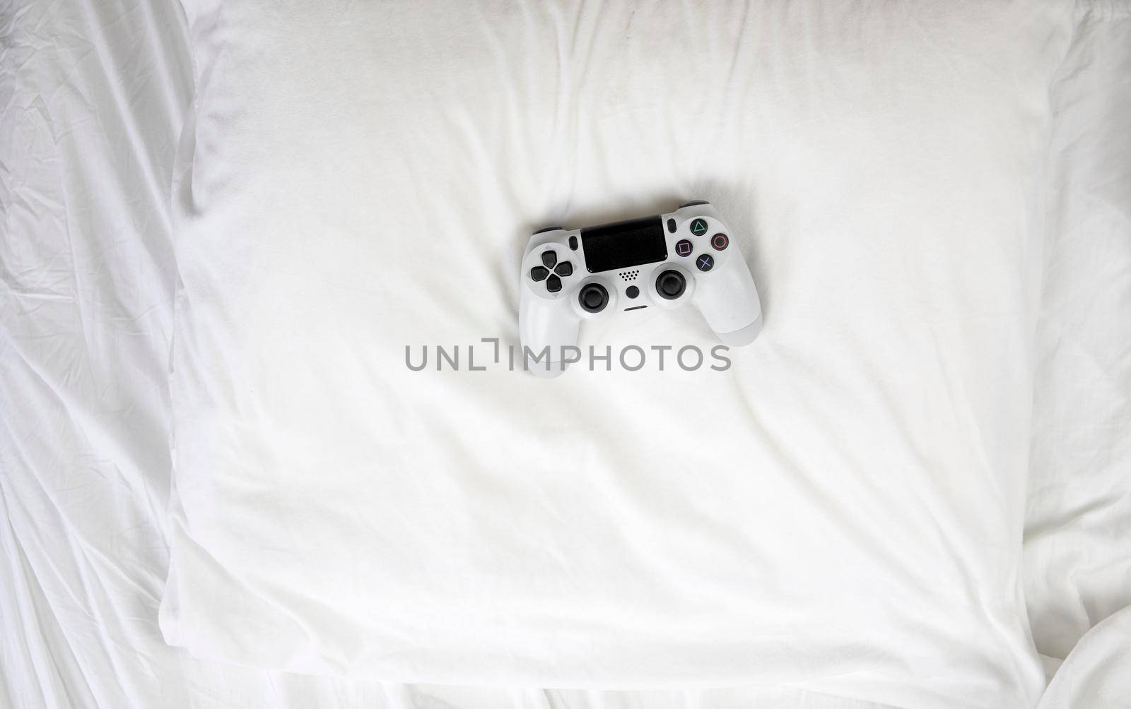 Closeup image top view game controller, lying on white sheets of bed at home with copy space concept