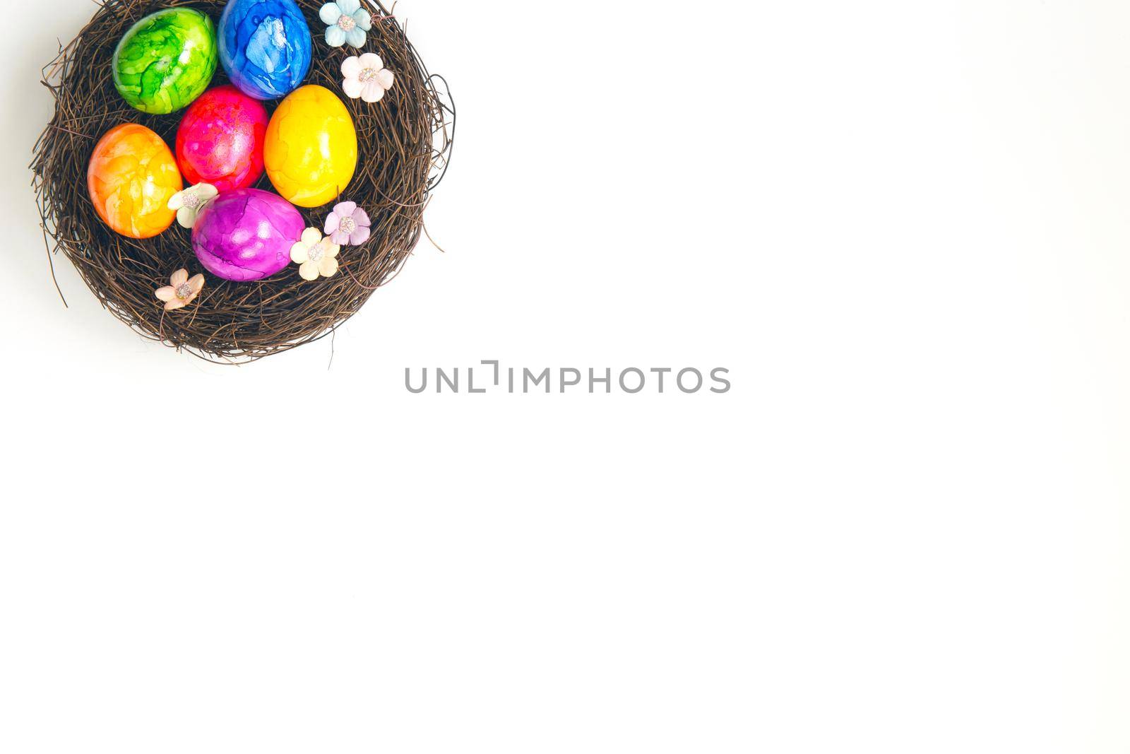 Colorful painted handmade Easter eggs in brown nest isolated on white background top view, Happy Easter holiday concept, with beautiful spring flowers copy space