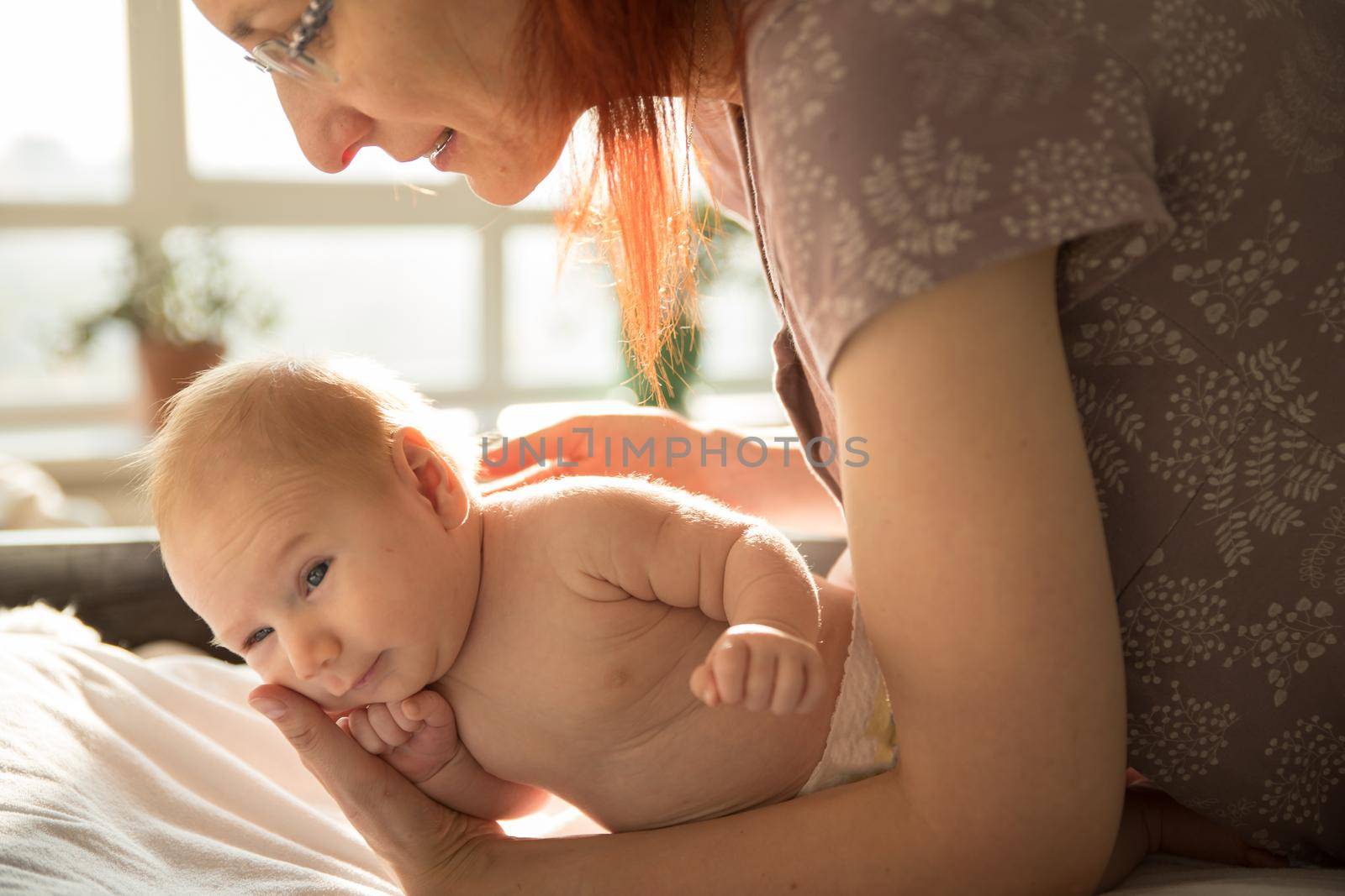 Mother holding her little baby lying on a bed. Mid shot