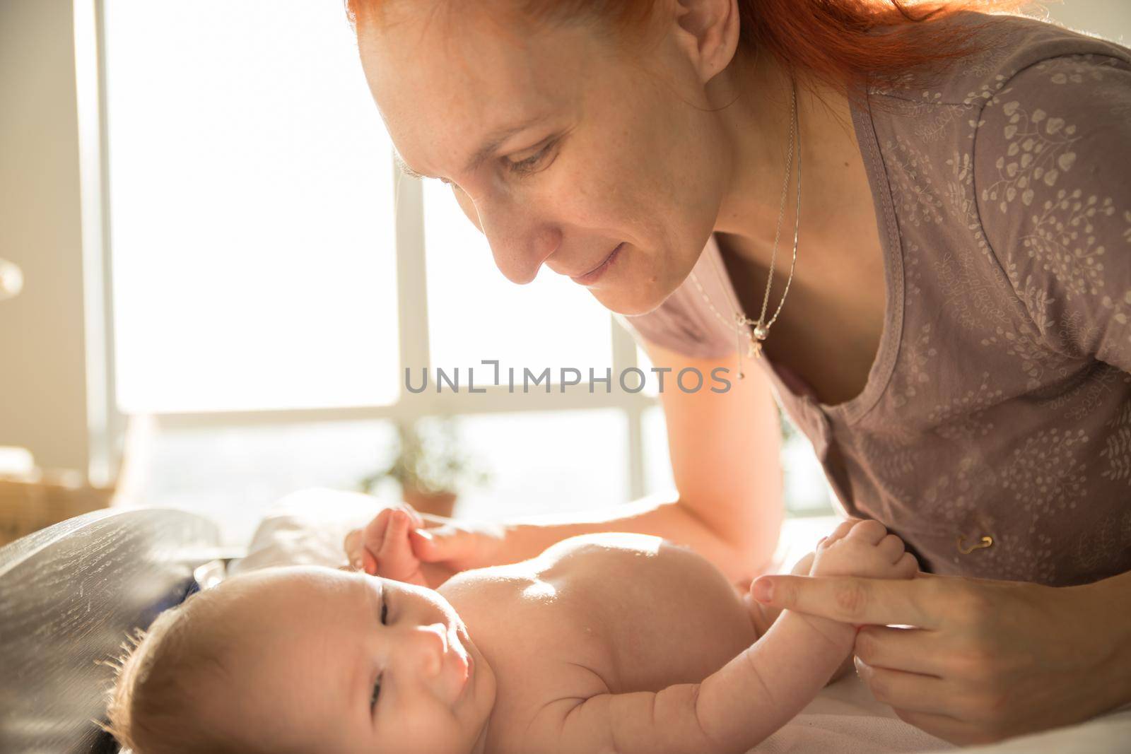 Smiling mother takes care of her small baby lying on a bed. Mid shot