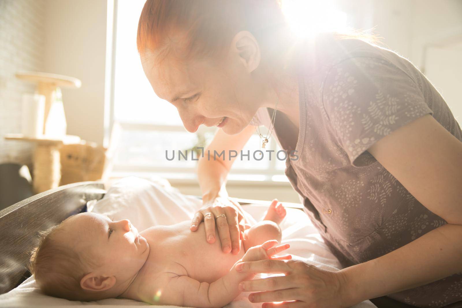 Smiling caring woman looking at her little baby with her hands on his stomach. Mid shot