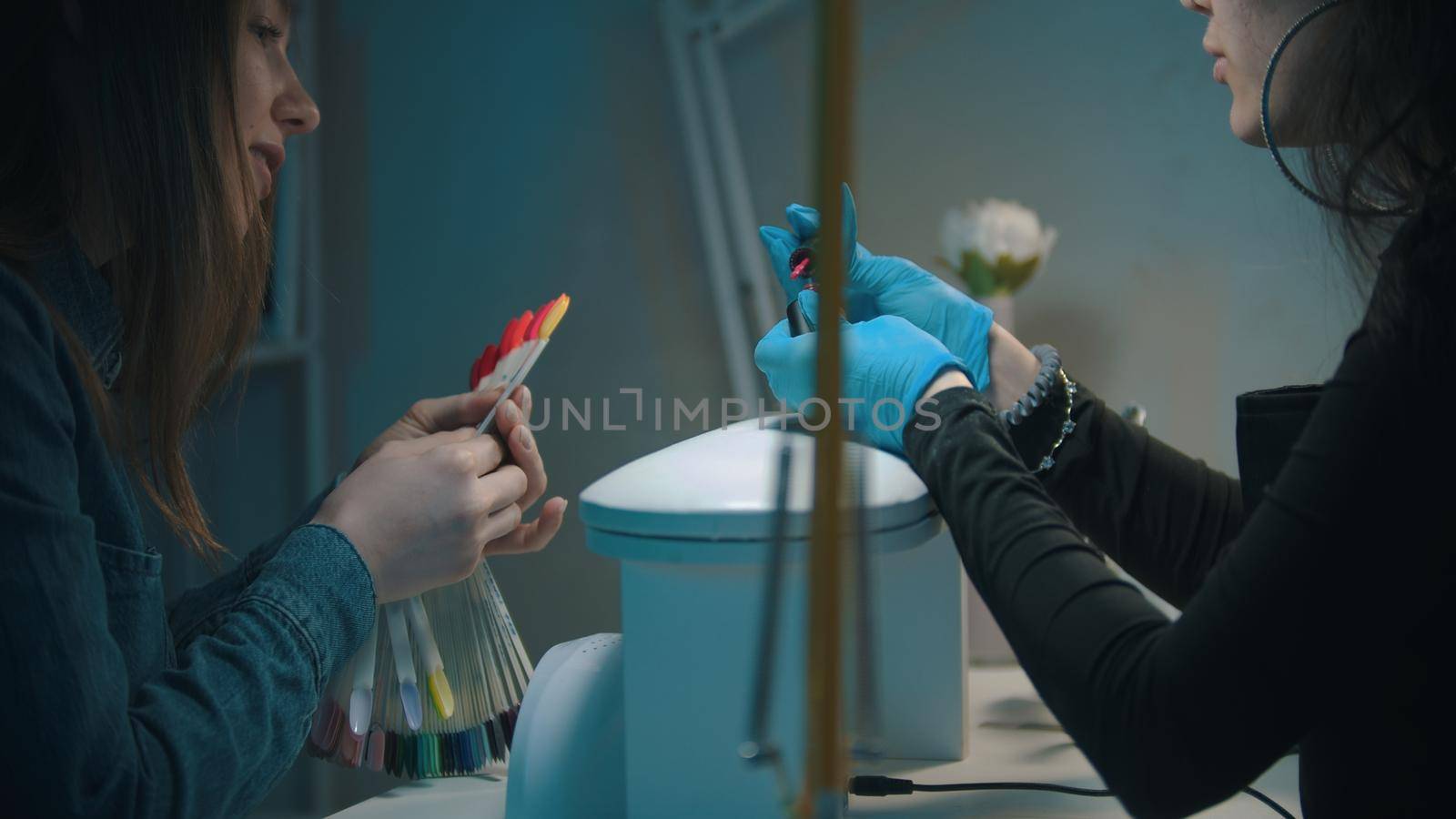 Manicure master and young woman choosing the color of nail polish on the samples. Mid shot