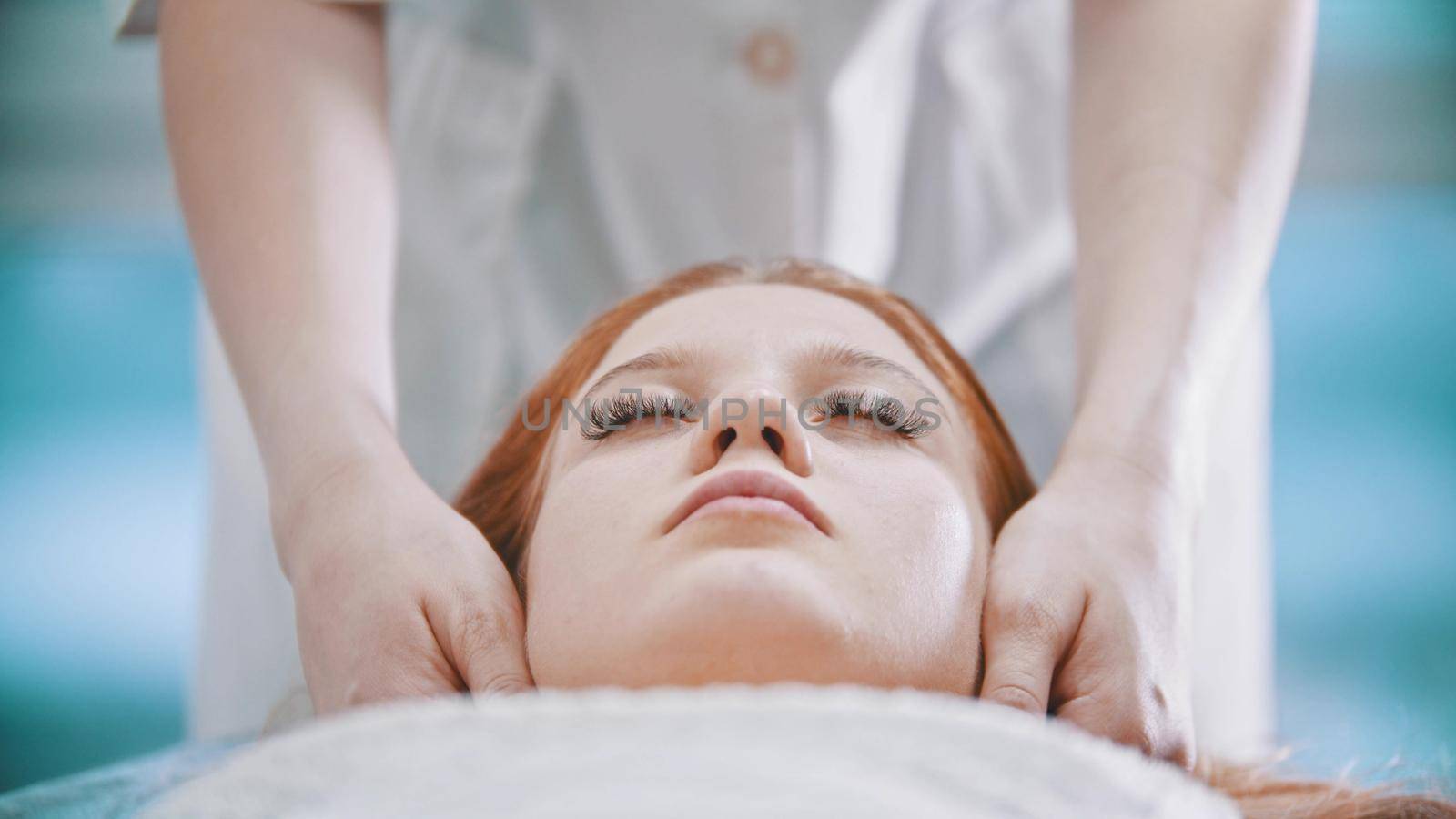 Massage - female masseuse kneading the chin area to a young woman using her palms - indoor