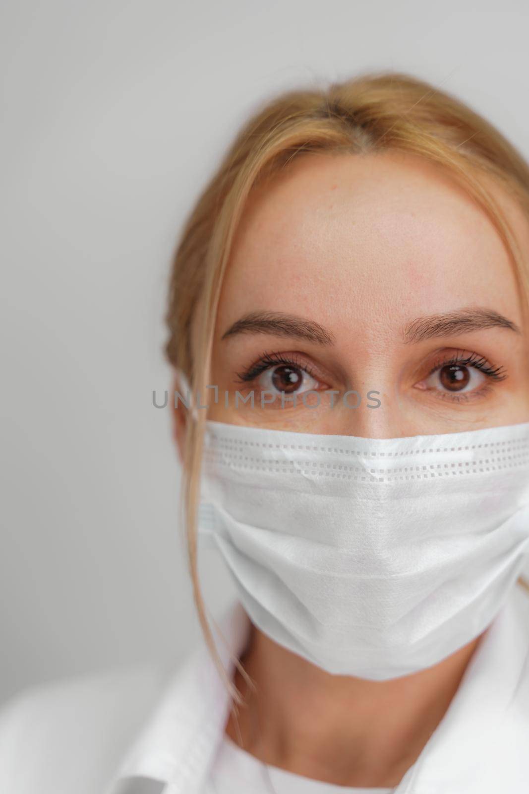 Close-up portrait of a young blonde woman in a medical mask on a light background. Virus protection. Coronovirus covid-19 The concept of a pandemic epidemic. Quarantine. Stay at home. by Matiunina