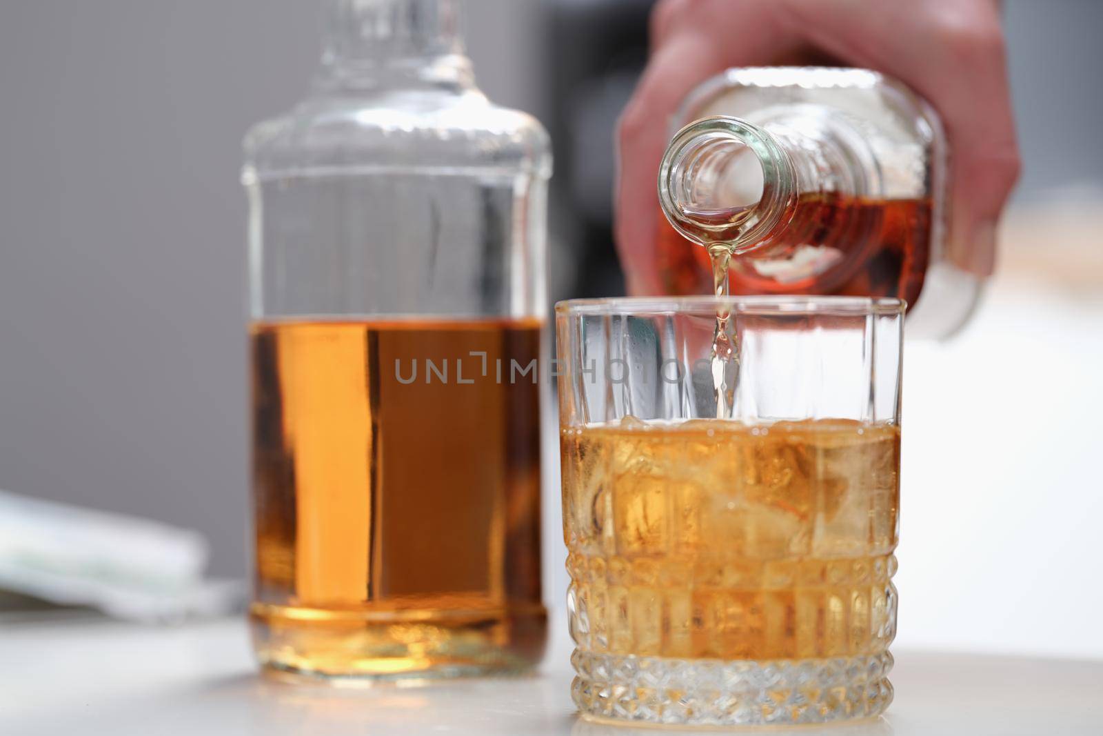 A hand pours alcohol from a bottle into a beautiful glass, close-up. Whiskey with ice, alcoholic cocktail, party