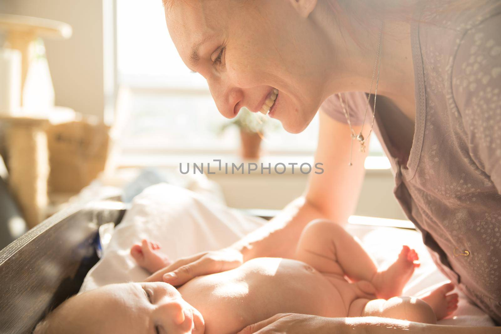 Smiling caring woman mother looking at her little baby. Mid shot