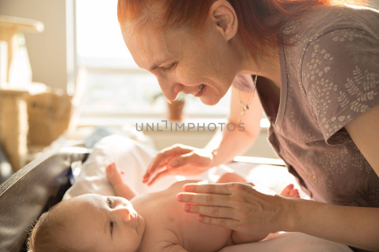 Smiling caring woman playing with her little baby. Mid shot