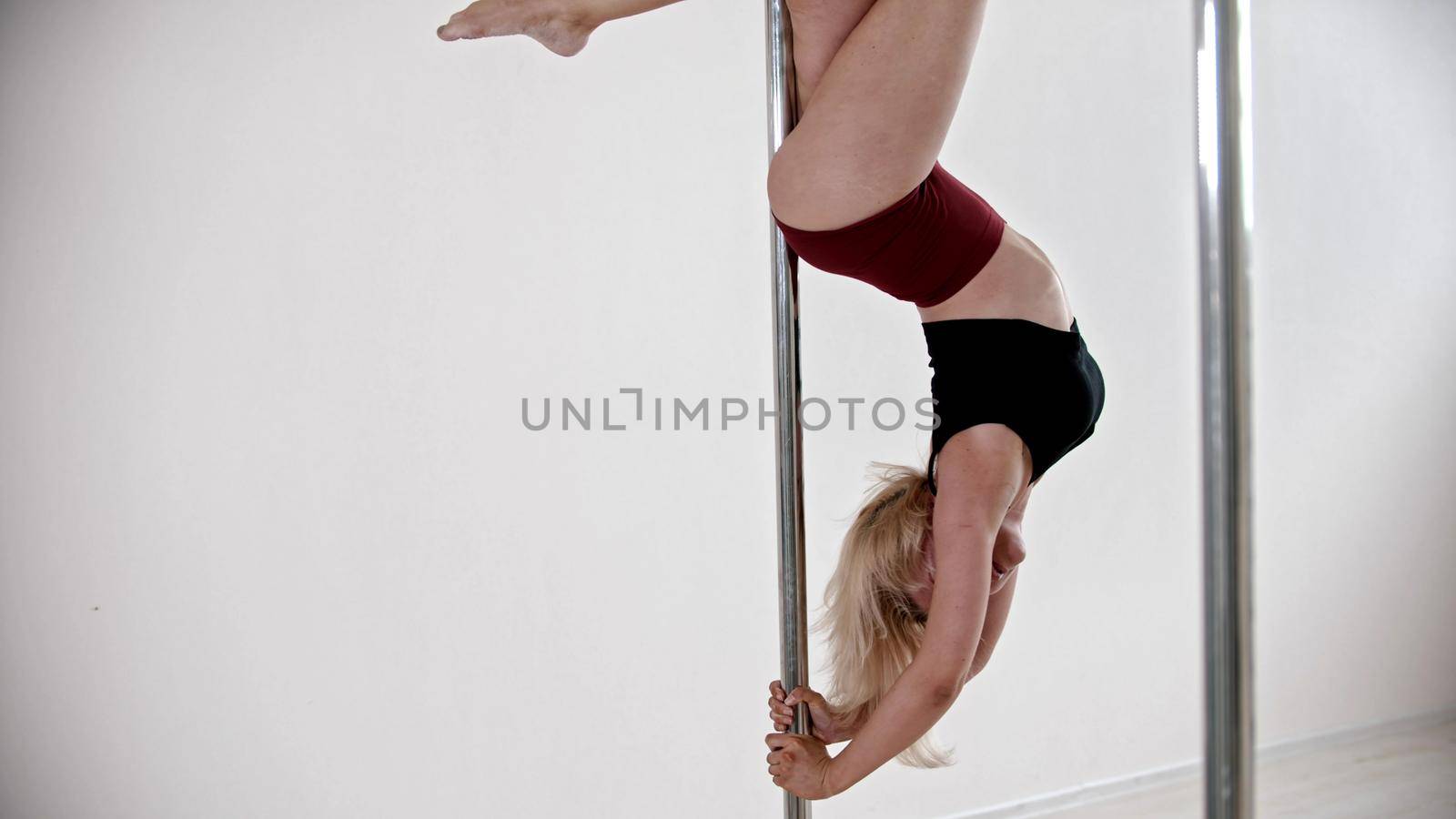 A blonde woman keeping the balance upside down on the pole. Mid shot