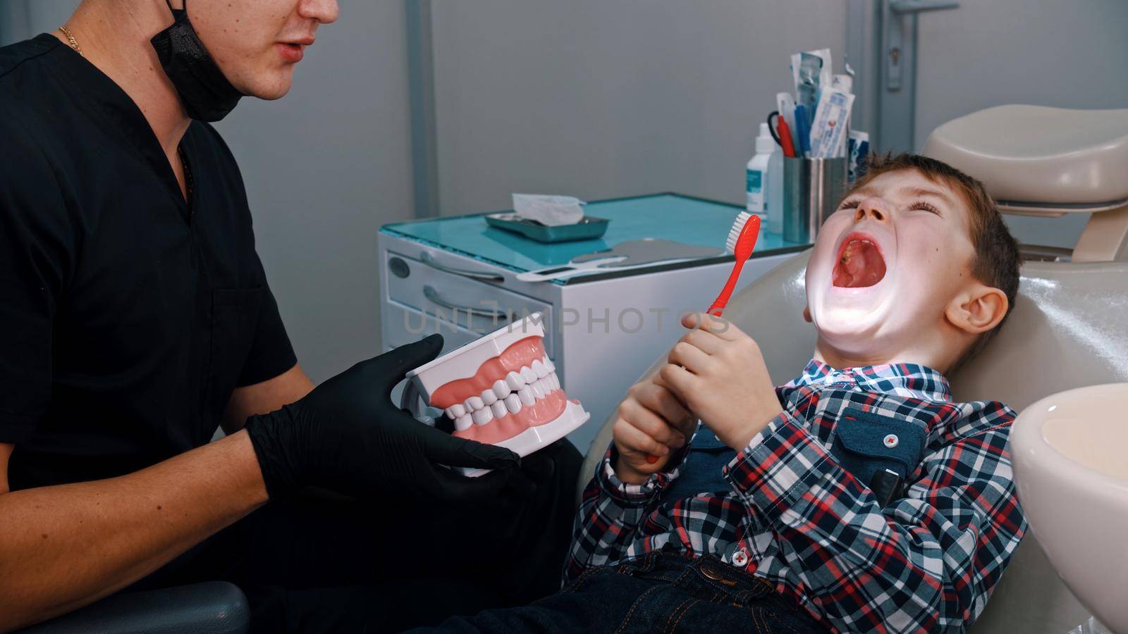 A little boy with opened mouth having a treatment in the dentistry - discuss the hygiene and brushing teeth. Mid shot