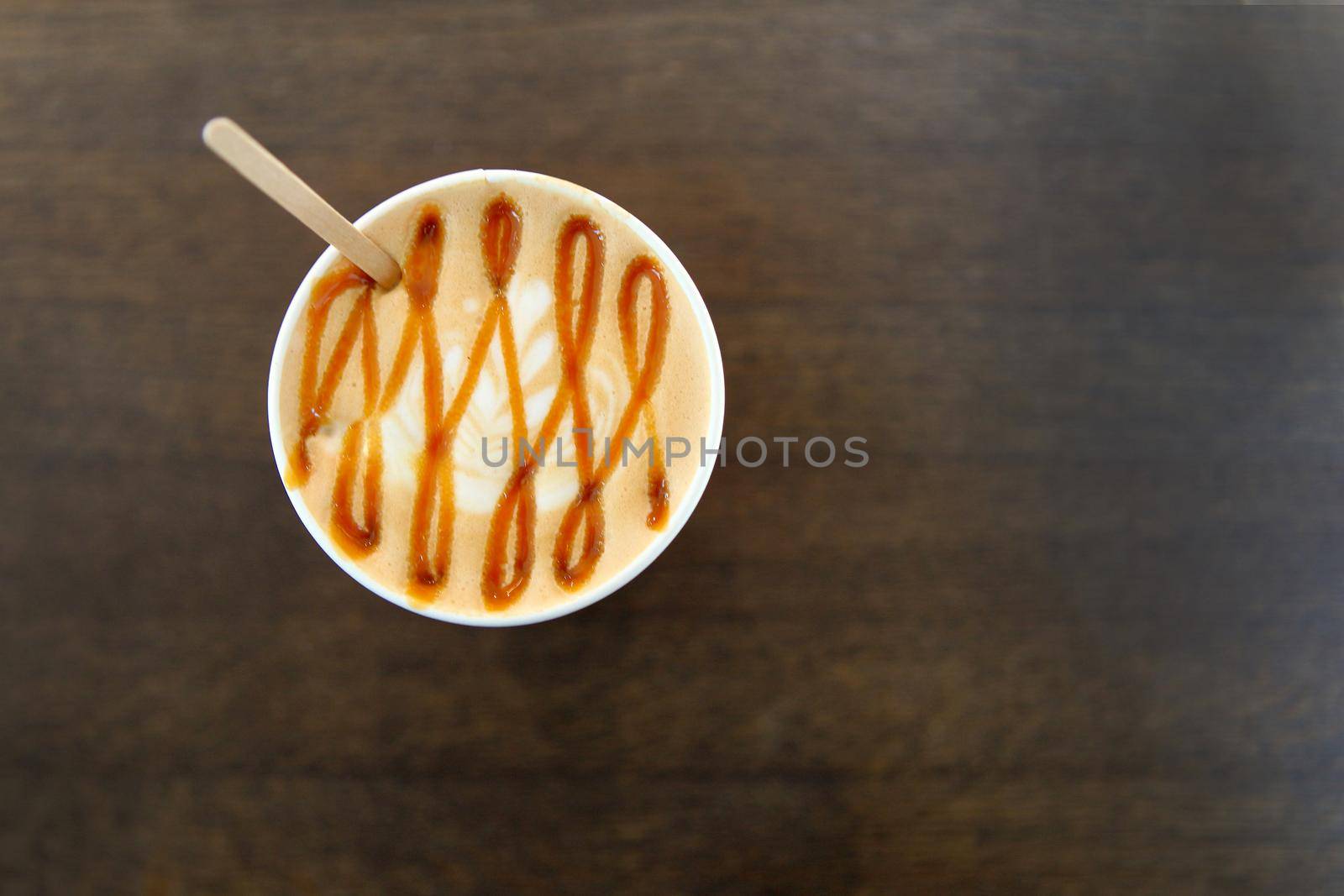 Caramel Big Coffee paper cup with milk on the wooden table. cappuccino or latte drink, cup of coffee on table flat lay view. Cup of cafe au lait. Milk paintings or latte art. Hot Coffee in mug