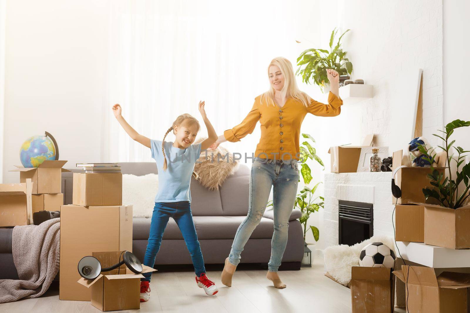 Pretty young mother and her cute little daughter having fun in new apartment and unpacking moving boxes