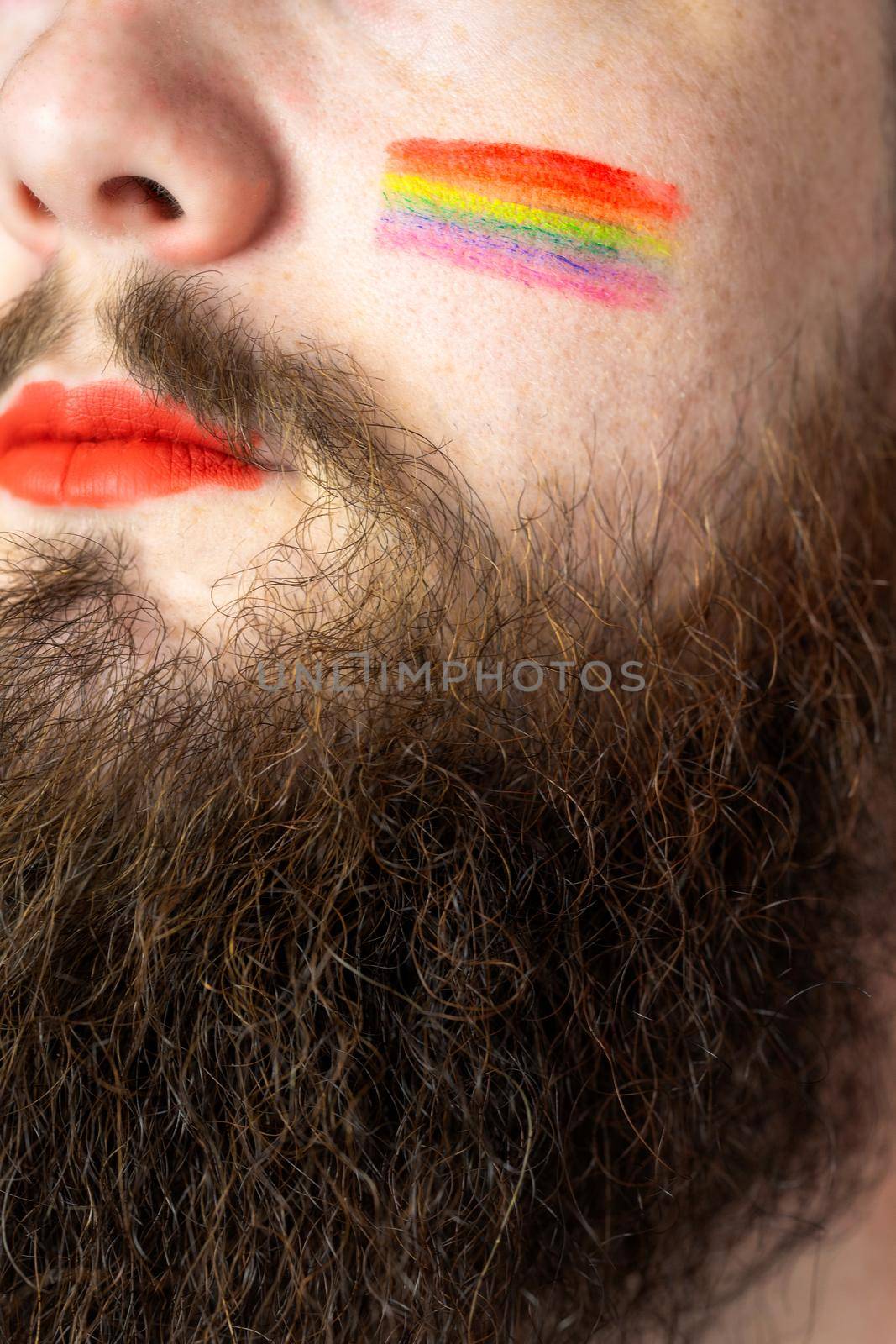 Young handsome bearded man with pride flag on his cheek, rainbow flag standing for LGBTQ, Gender right and sexual minority. Portrait closeup