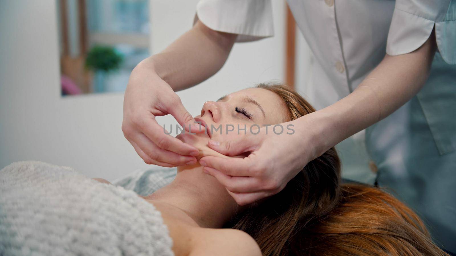 Massage - woman massage therapist massaging the face of a red-haired woman with her hands - indoor