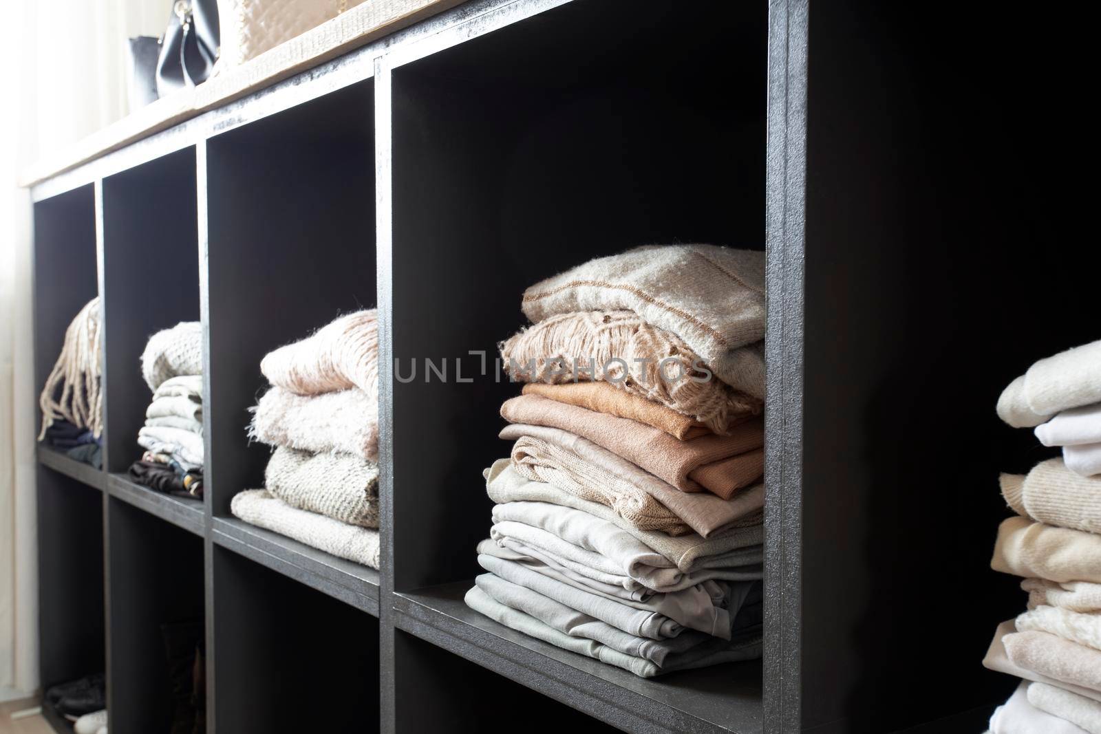 Open wardrobe with lots of folded clothes, organized closet with piled up clothes modern and clean interior of luxury home closeup