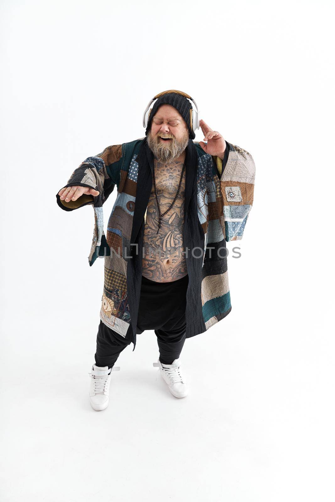 Fat stylish bearded tattoed caucasian man with big belly is posing and dancing wearing ethnic kimono