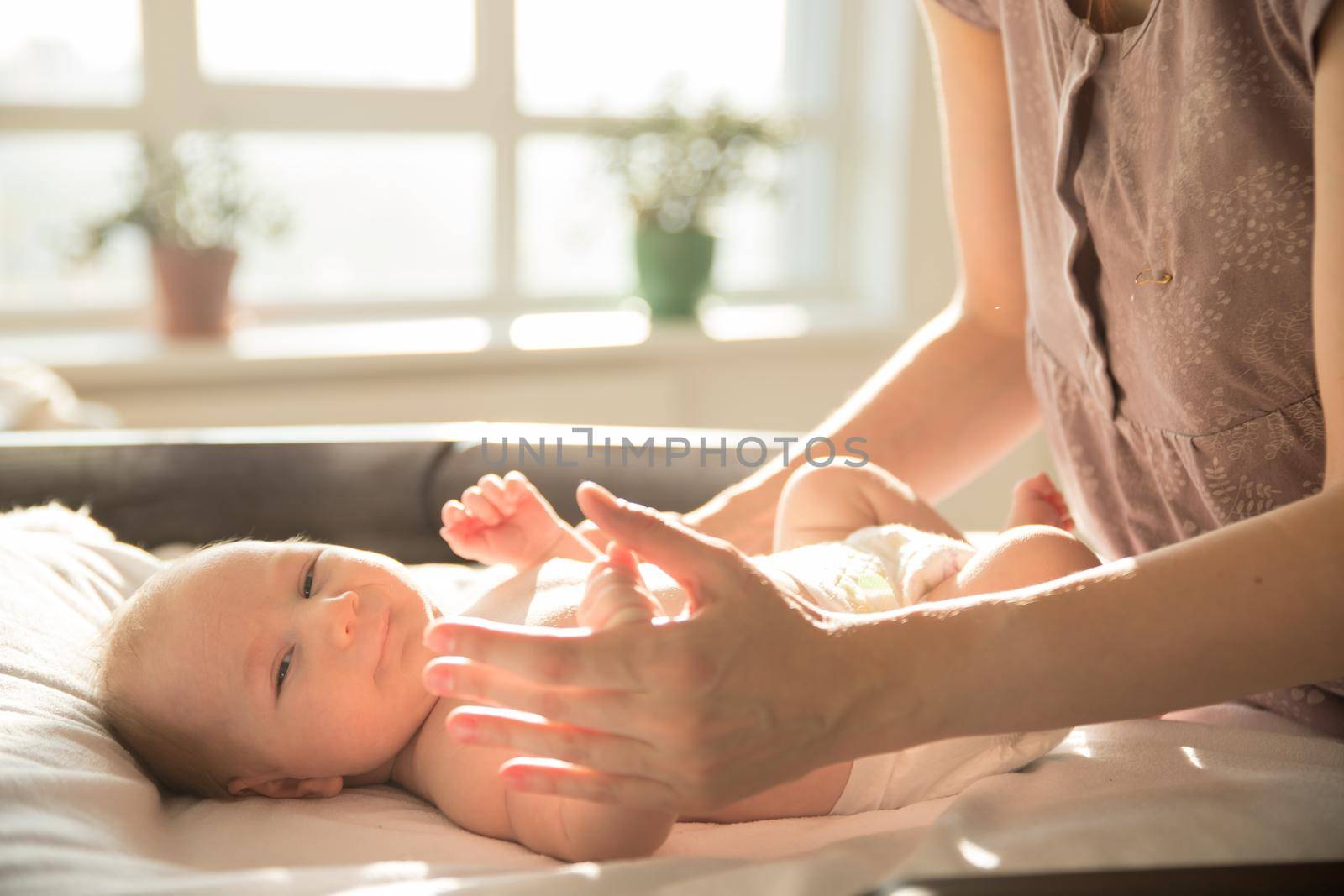 Mother takes care of her little baby lying on a bed. Mid shot