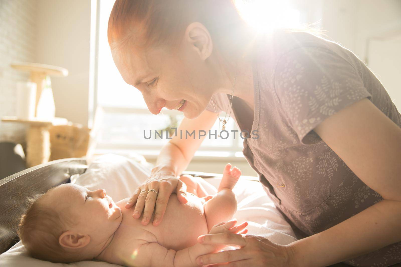 Smiling caring mother looking at her little baby with her hands on his stomach by Studia72