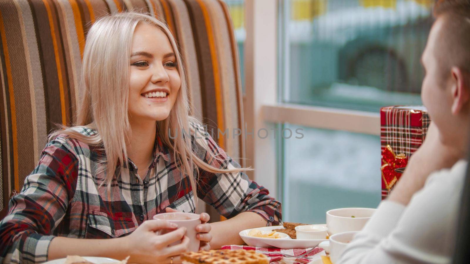 A young woman drinks coffee and talking with her boyfriend in cafe. Mid shot