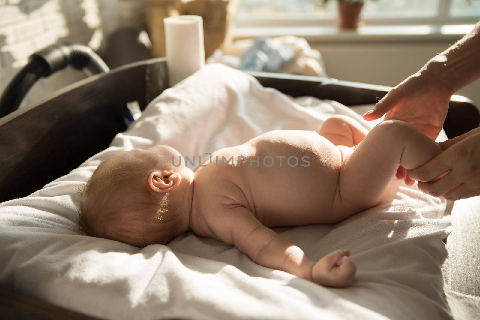 A little baby lying on a bed on white sheets and his parent holding his legs. Mid shot