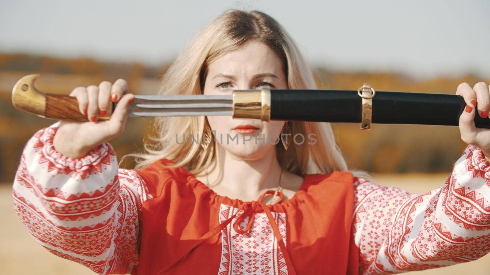 Feisty woman in red dress pulls out a sword out of the sheath. Mid shot